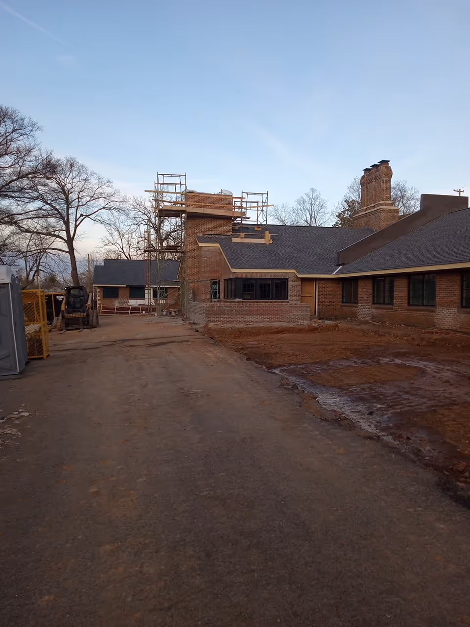Exterior brick building under construction with scaffolding and a dirt foreground.