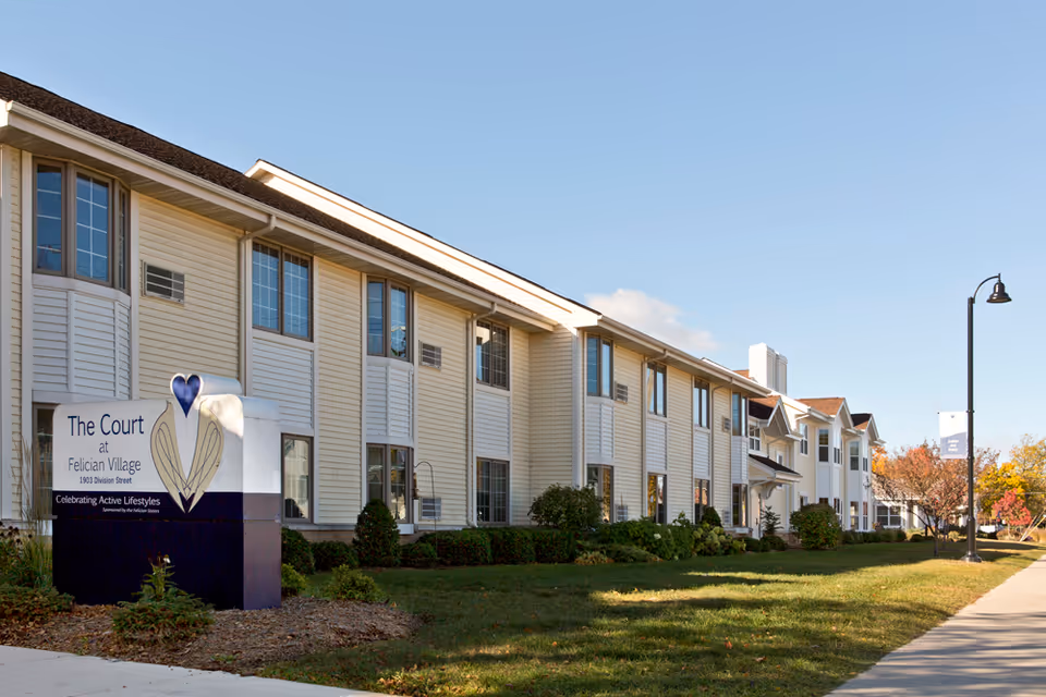 Exterior view of a senior living building with a front sign and a manicured lawn.