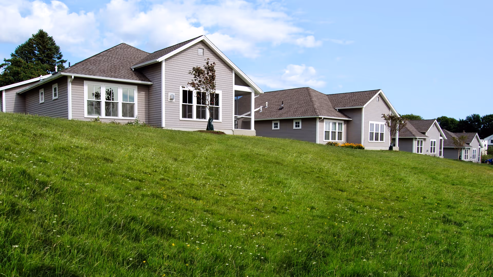 Row of single-story beige townhouses on a grassy hill under a blue sky