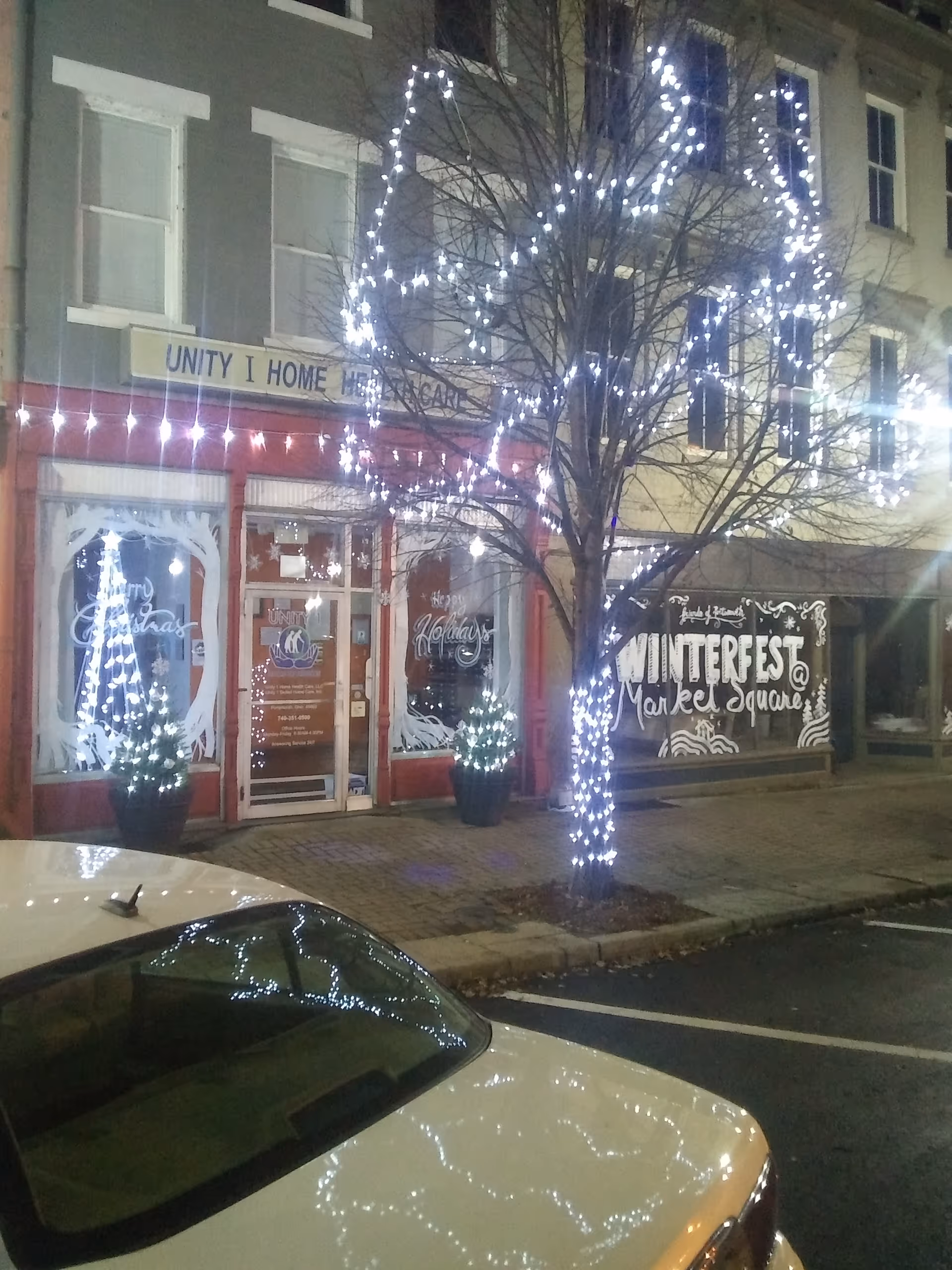 Night exterior of Unity 1 Home Health Care storefront with holiday lights wrapped around trees