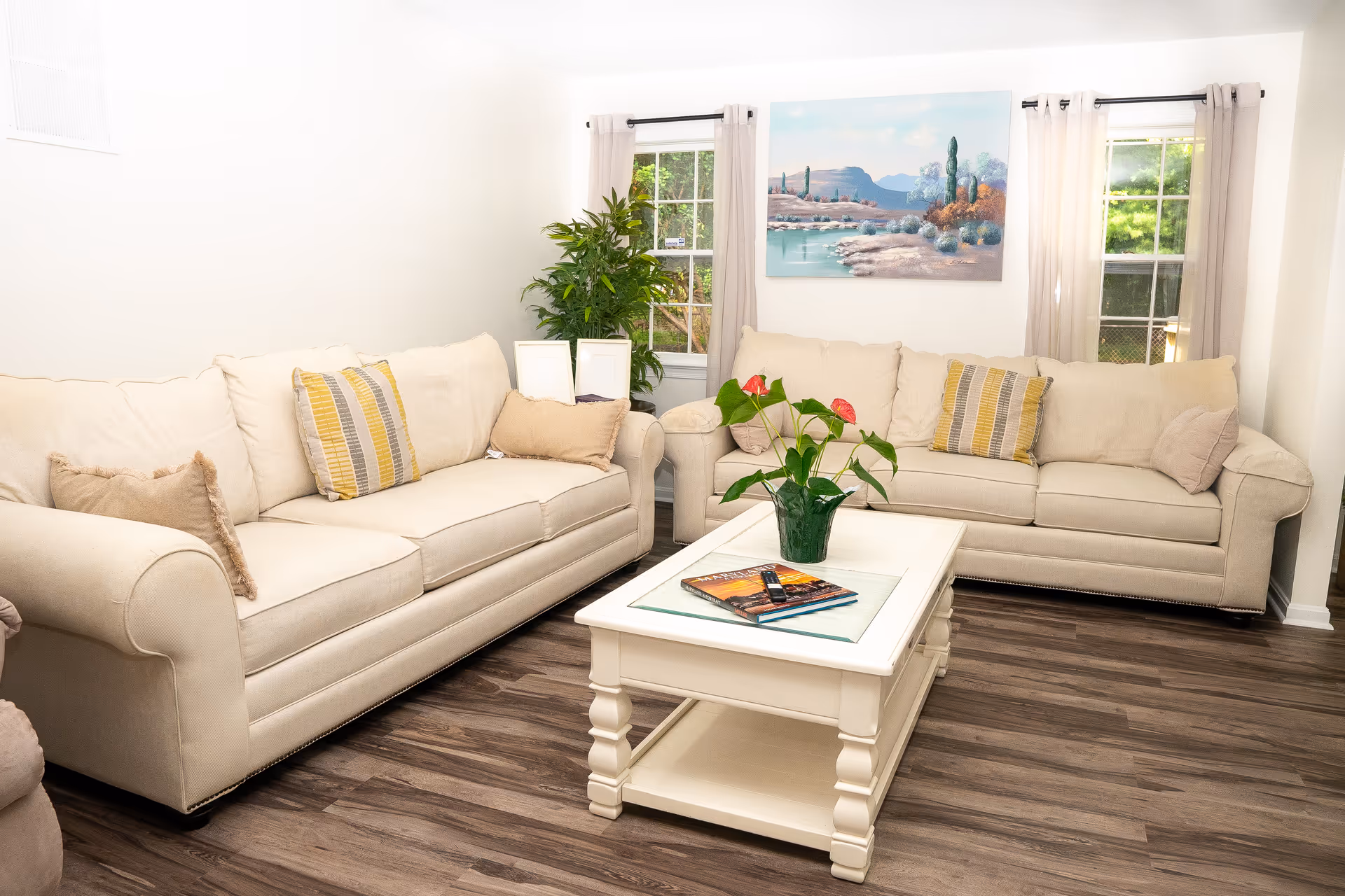 Bright beige living room with two sofas, a coffee table, plants, and wall art.