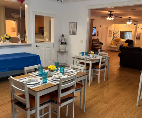 Dining room in a senior facility with set tables, teal glasses, and yellow centerpieces.