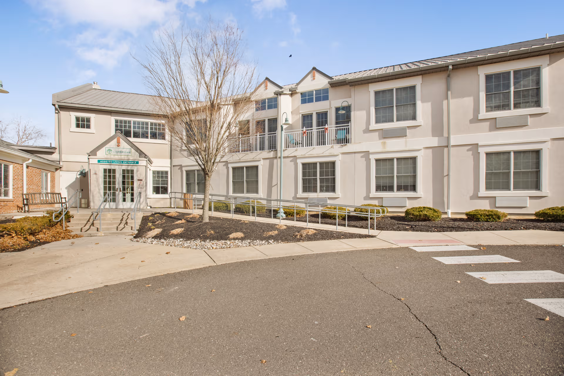Two-story light-colored senior living facility exterior with entrance and ramp
