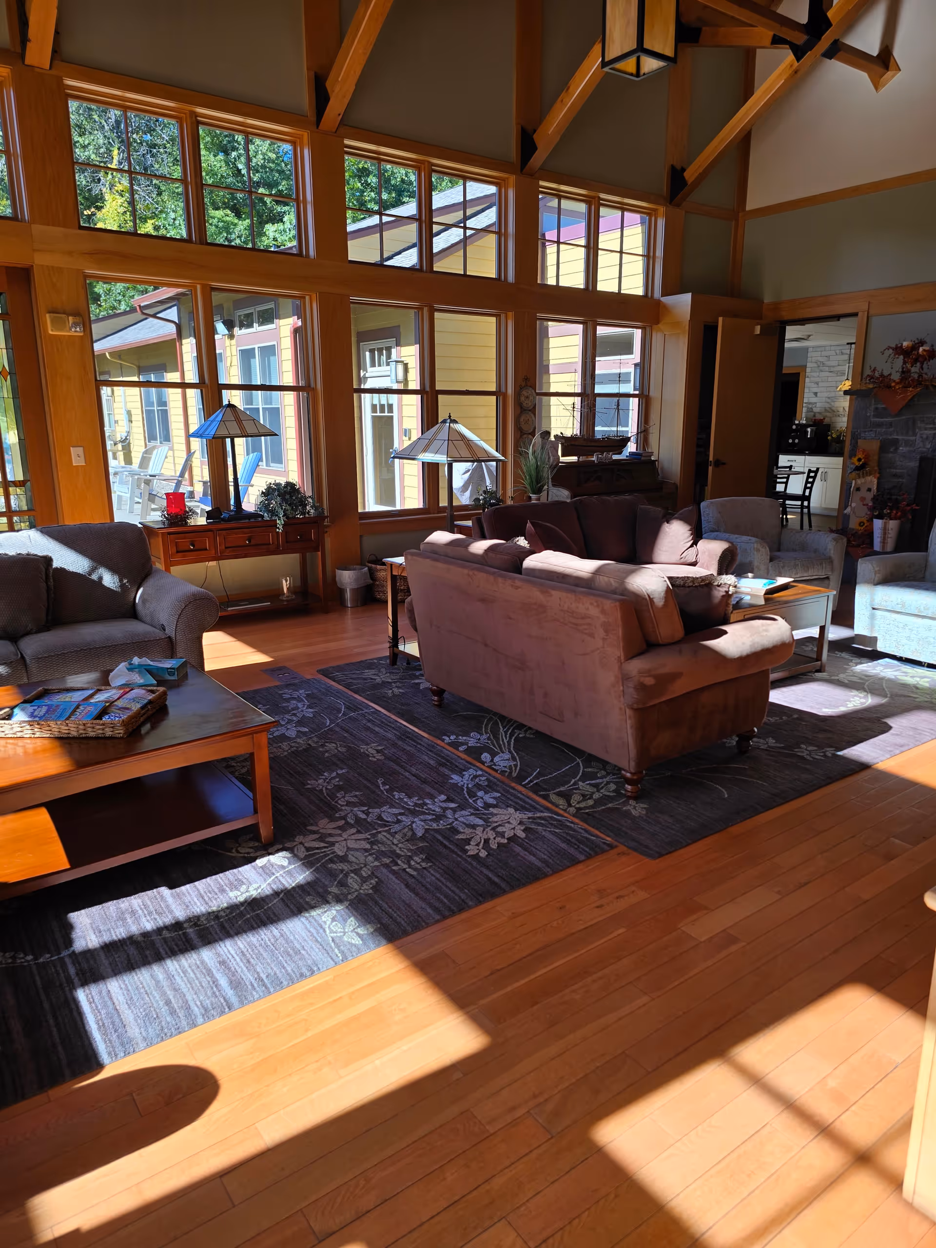 Bright living room with wooden beams, large windows, and tan couches arranged around coffee tables.