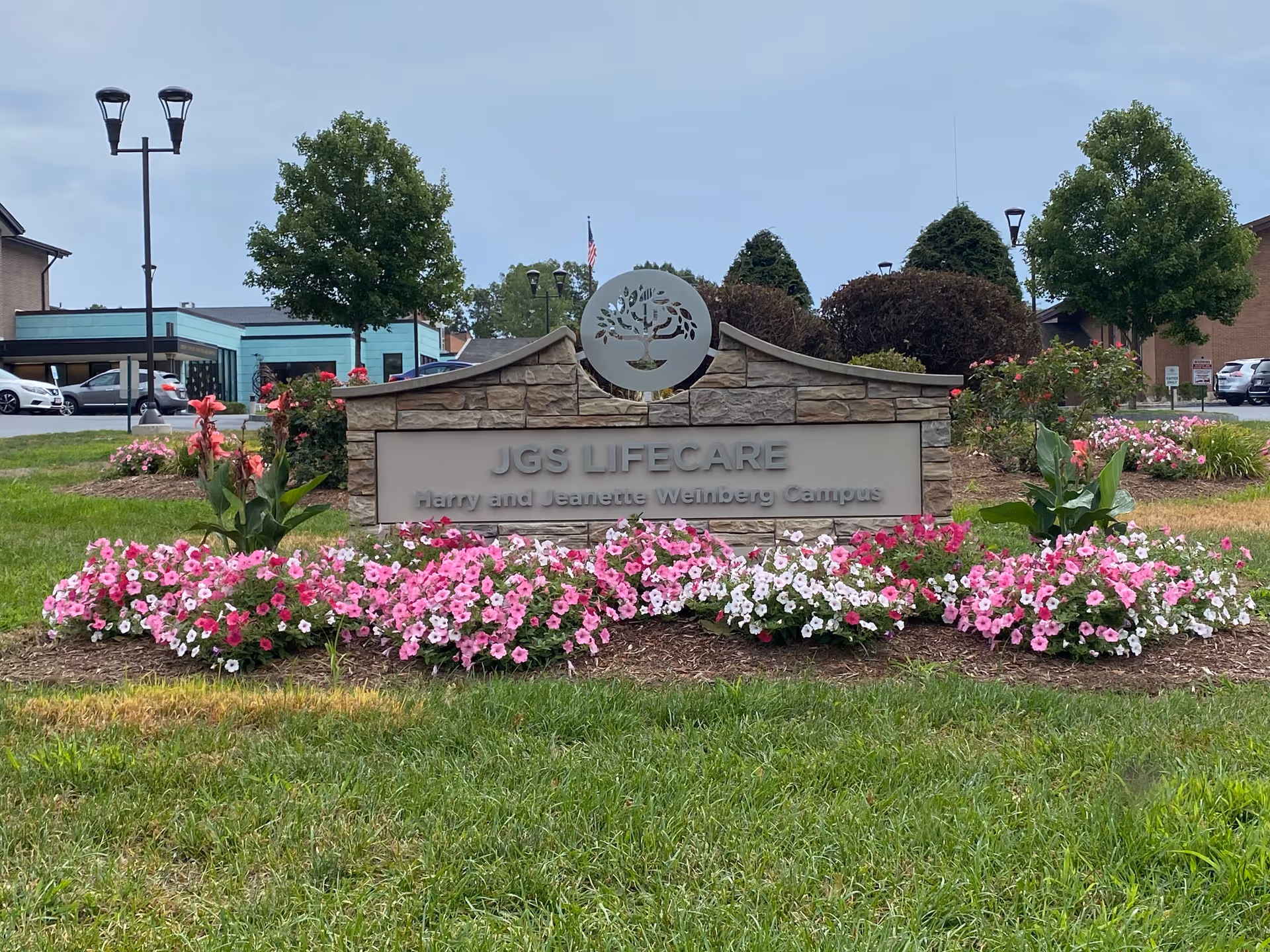 Exterior stone sign with JGS Lifecare surrounded by pink and white flowers.