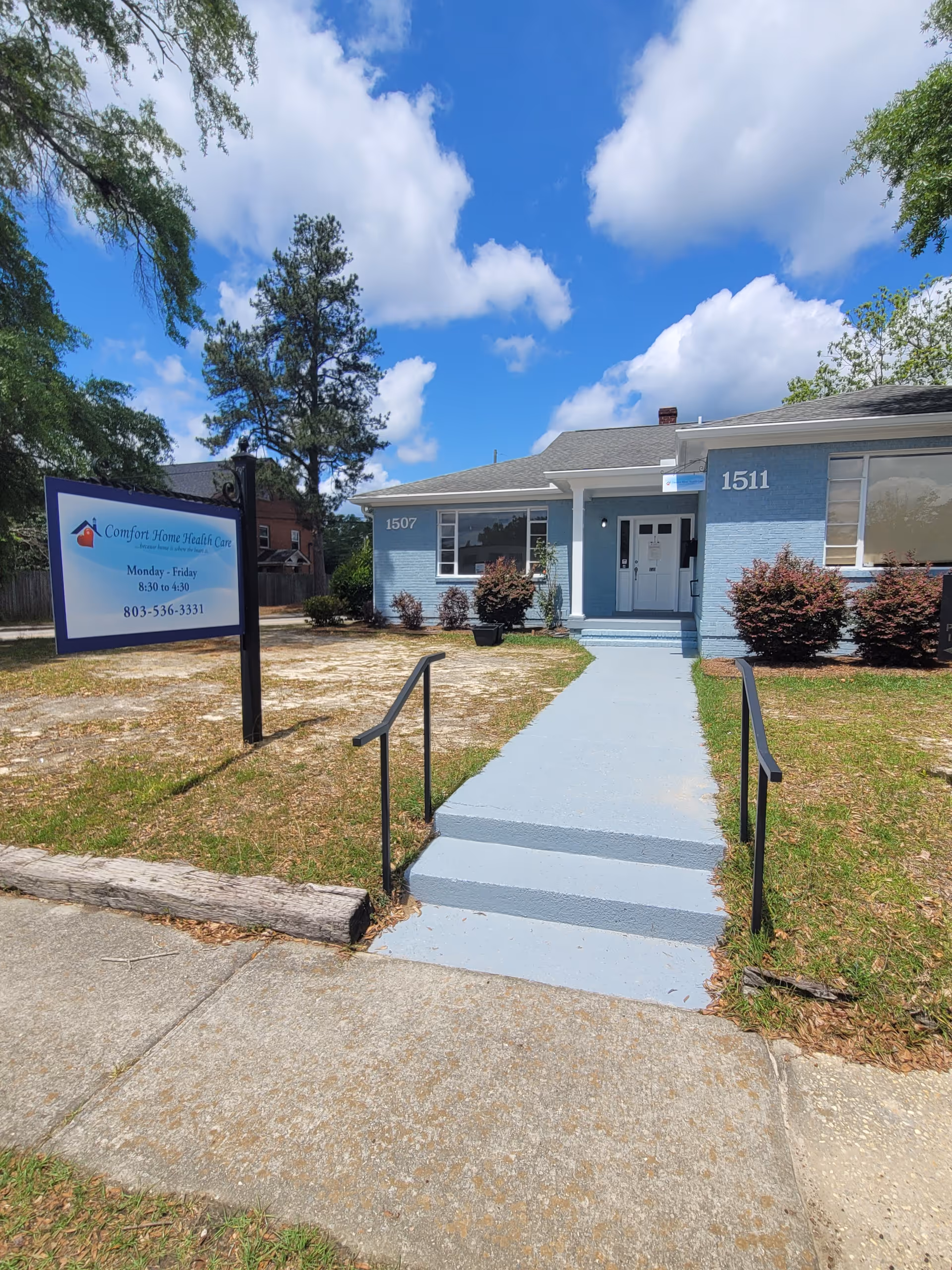 Front exterior of a blue Comfort Home Health Care building with stairs and a sign.