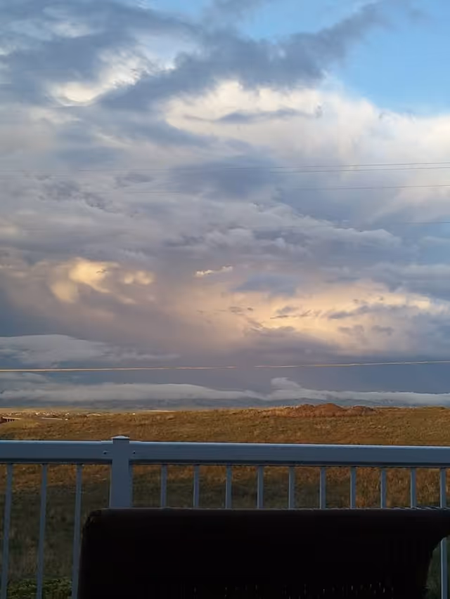 View from a balcony overlooking a grassy field with a cloudy sky above.