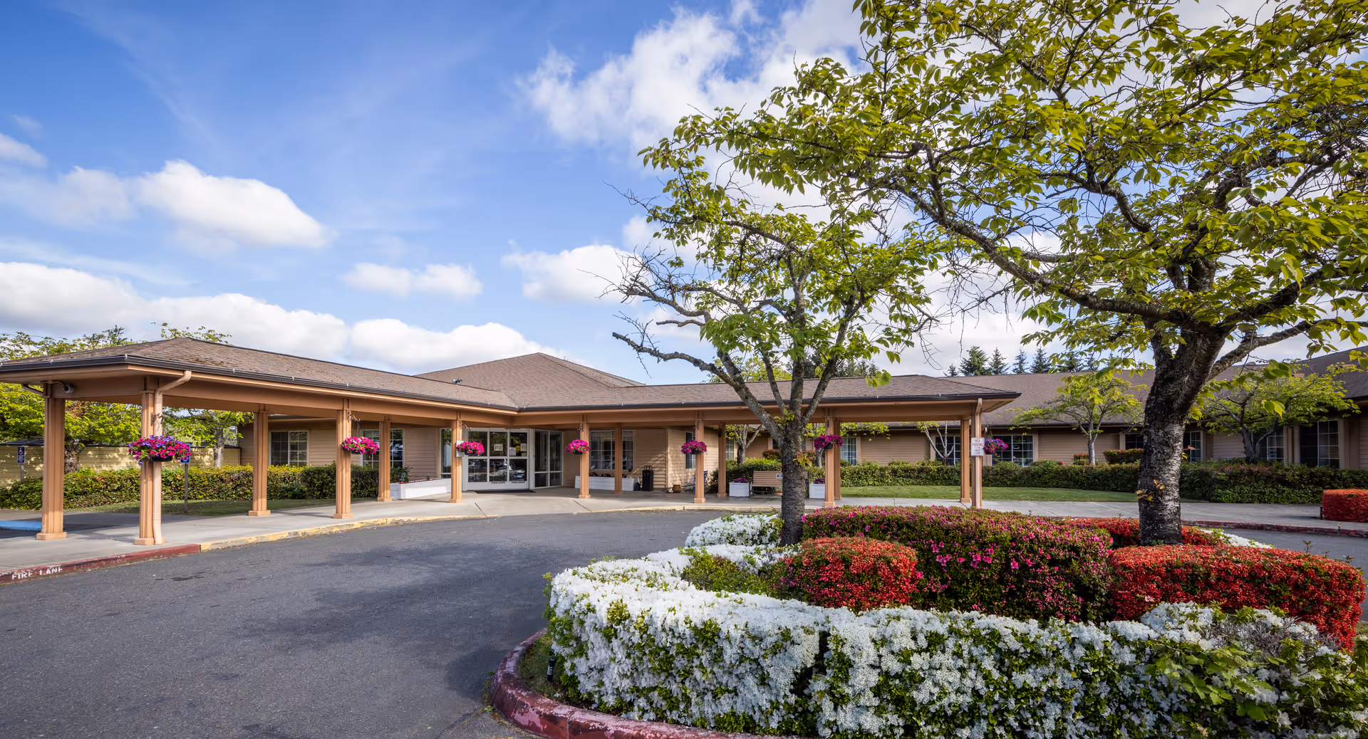 An exterior view of Alaska Gardens Health and Rehabilitation Services, featuring landscaped flower beds and trees in the forefront.