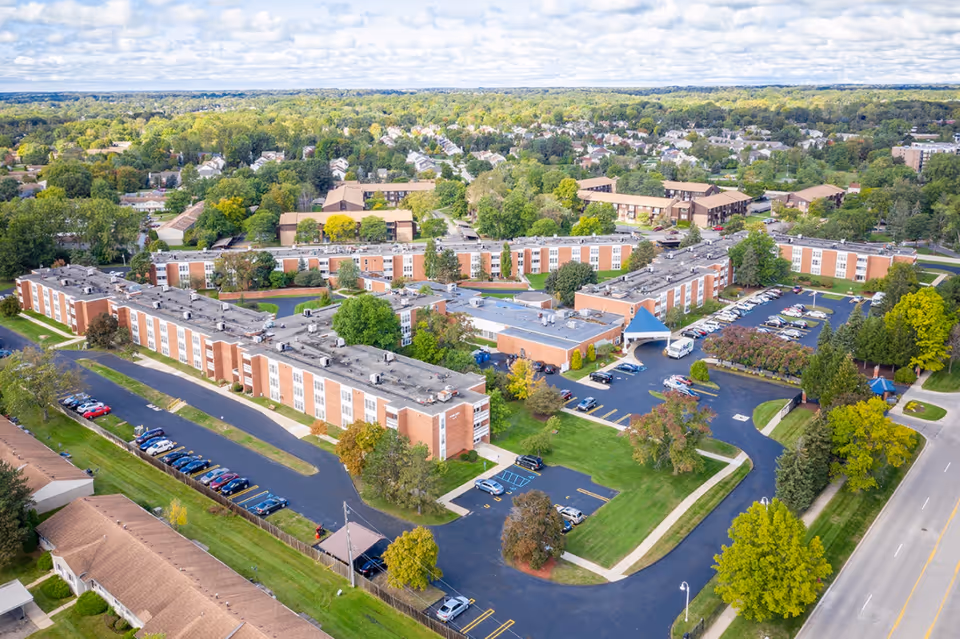An aerial view of a senior living campus with brick buildings, parking lots, and trees.