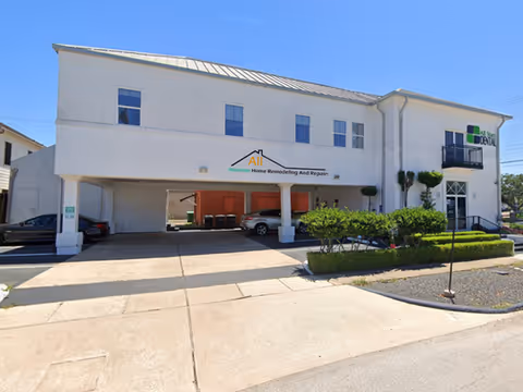 Two-story white building with a covered entrance, signage, and parked cars in front.
