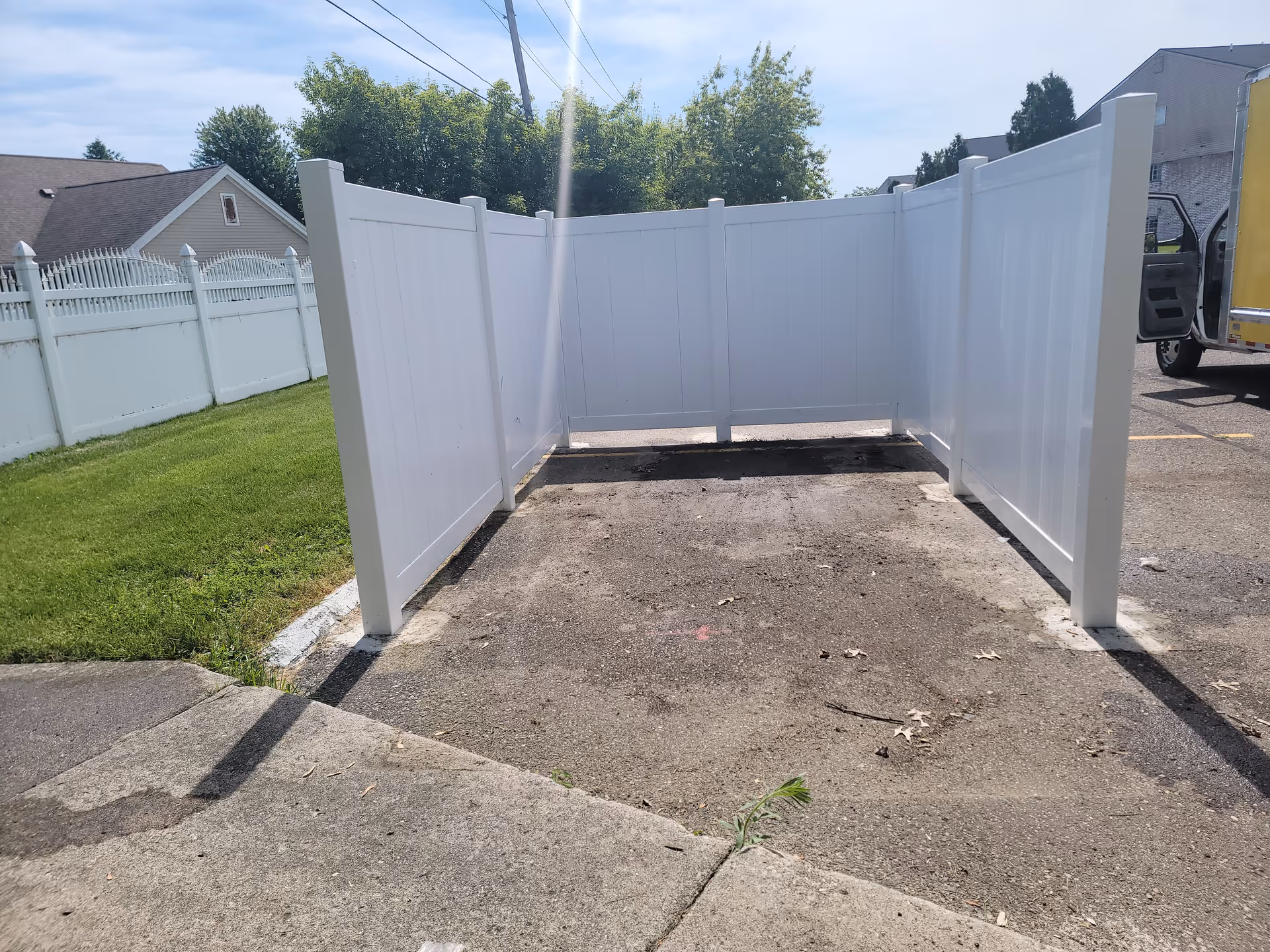 White vinyl privacy fence encloses a small outdoor concrete area adjacent to a driveway.