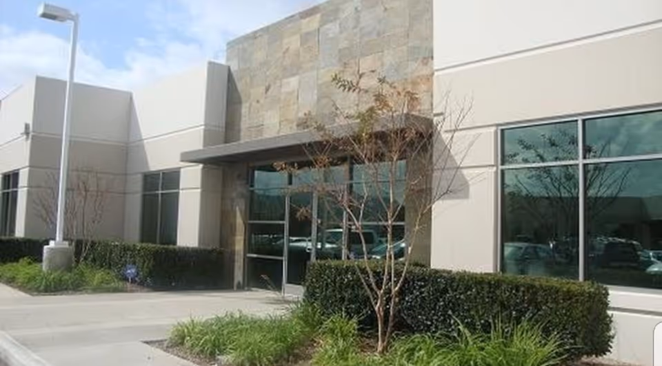 Exterior view of a modern senior living facility entrance with glass doors and landscaping.