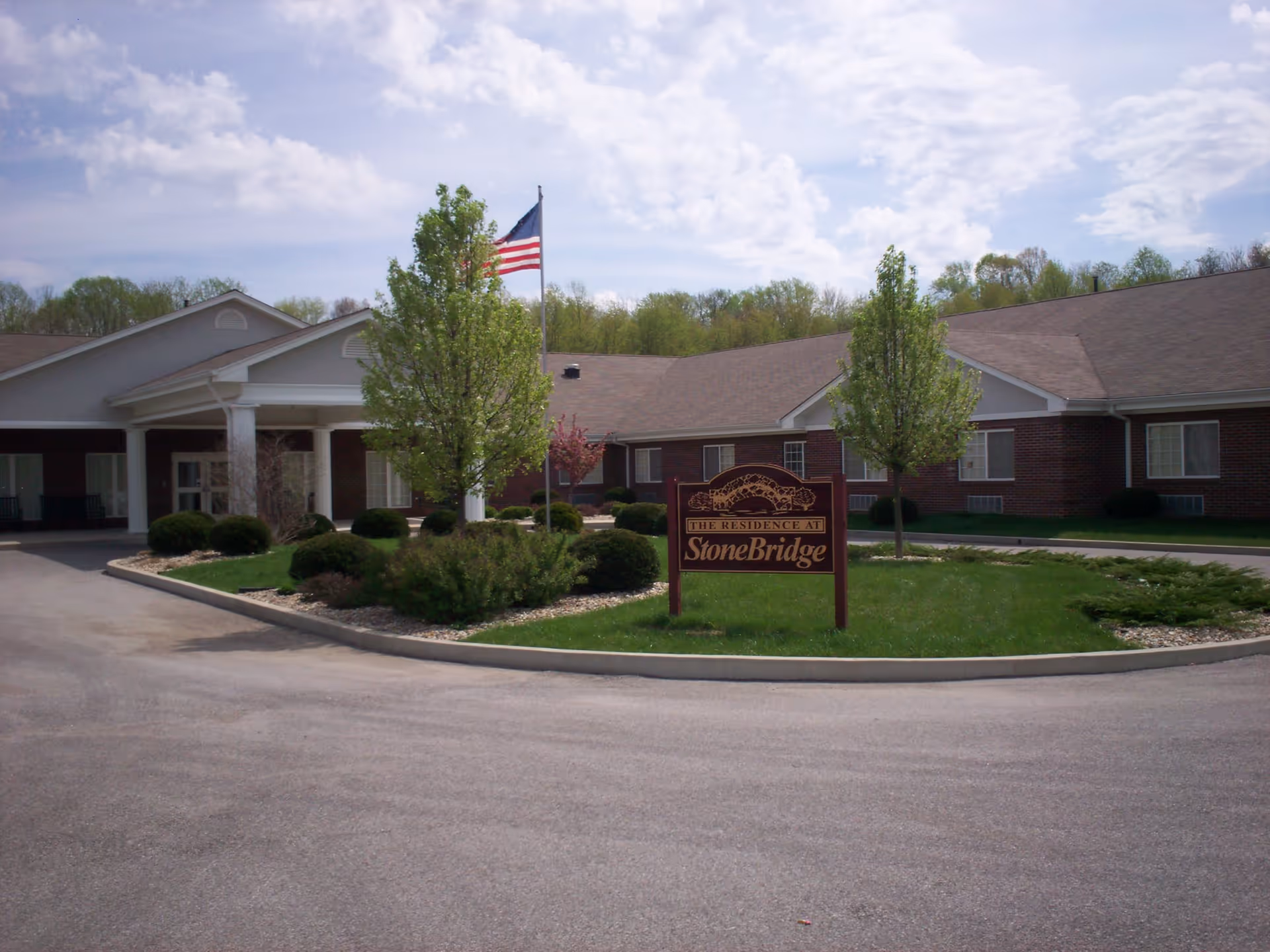 Front entrance of a single-story brick senior living building with a StoneBridge sign and an American flag.