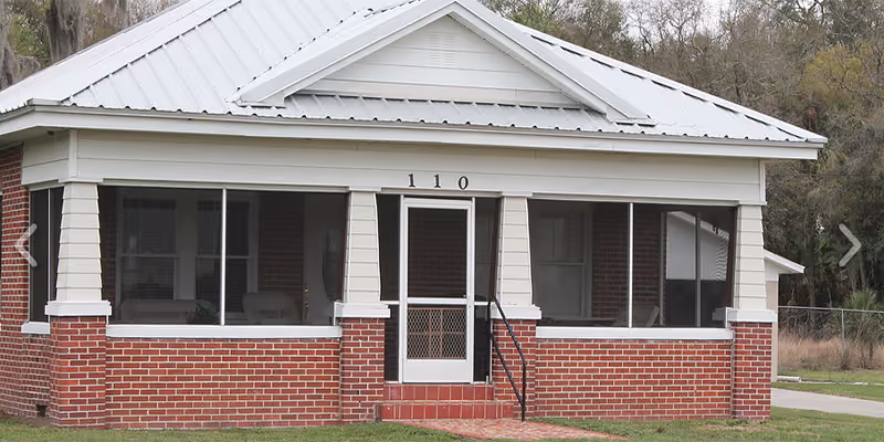 Single-story brick building with white trim, screened front porch, and metal roof; address 1110.