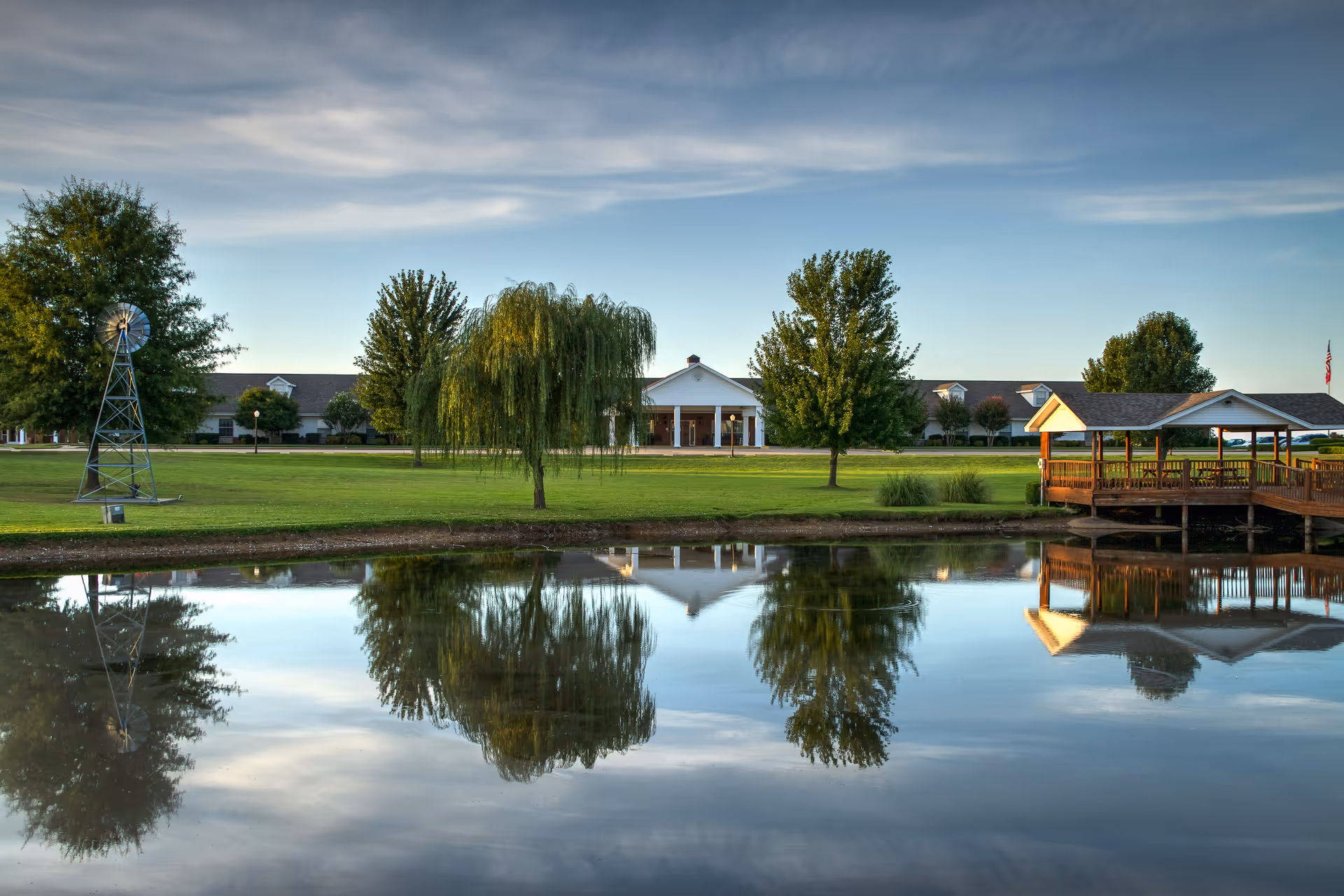 Exterior view of Greenhurst Nursing Center with a pond, trees, and a wooden pavilion.