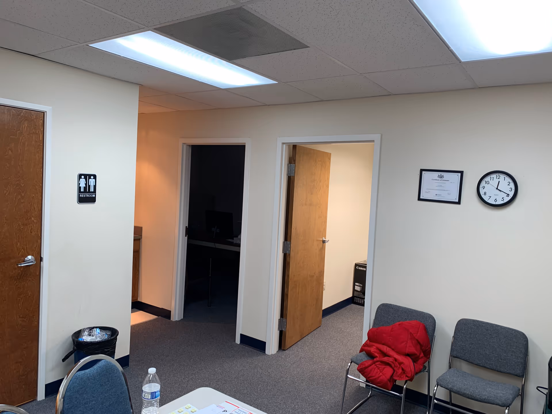Interior hallway of a senior living facility with doors, chairs, clock, and restroom sign.