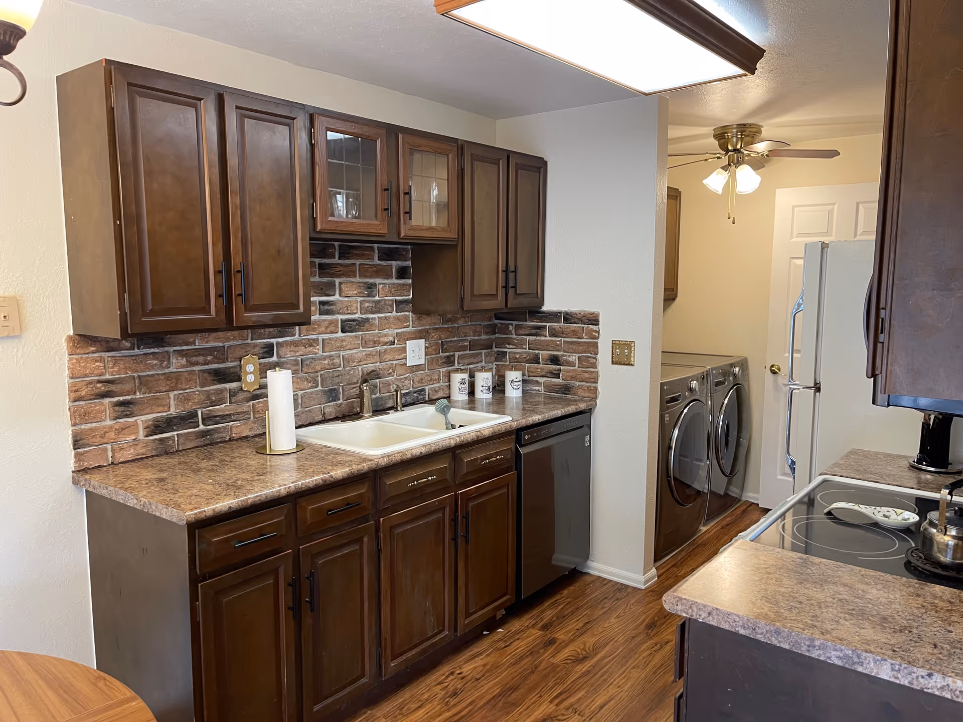 Dark wood kitchen cabinets with brick backsplash, sink, and adjacent laundry area with appliances.
