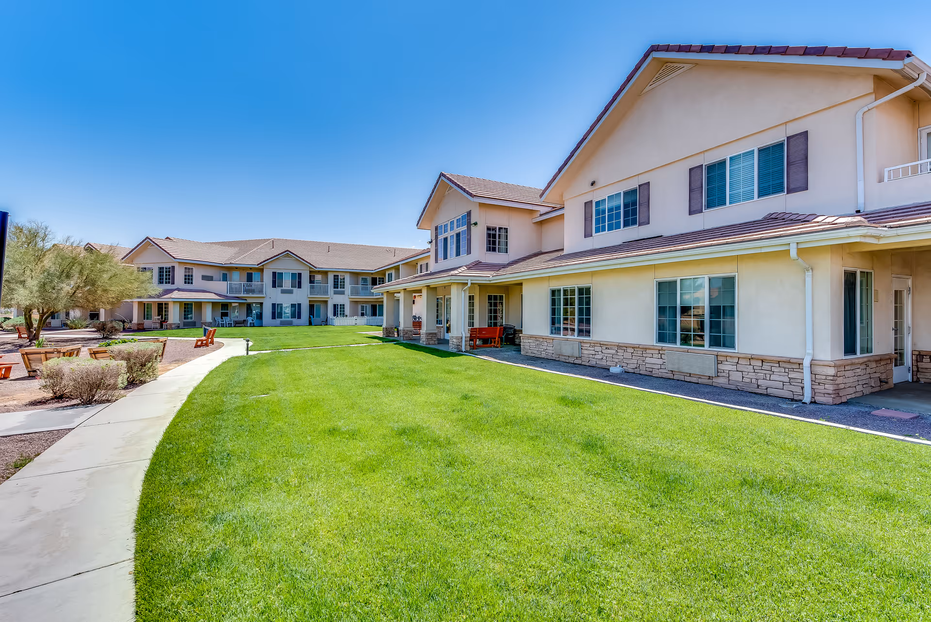 A senior living campus with beige buildings, a manicured lawn, and a clear blue sky.