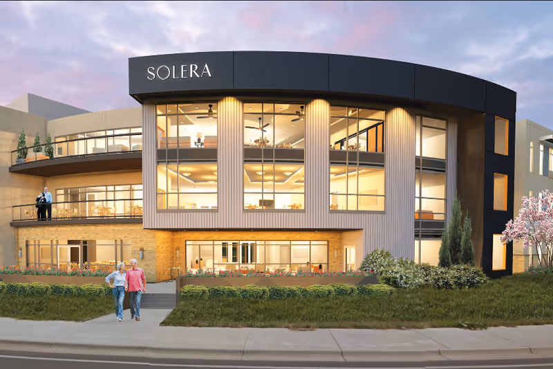 Front exterior of a modern Solera senior living facility with glass walls and curved black facade.