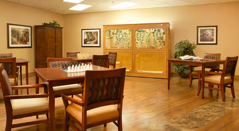Interior common room in a senior facility with tables, chairs, a chessboard, and art.