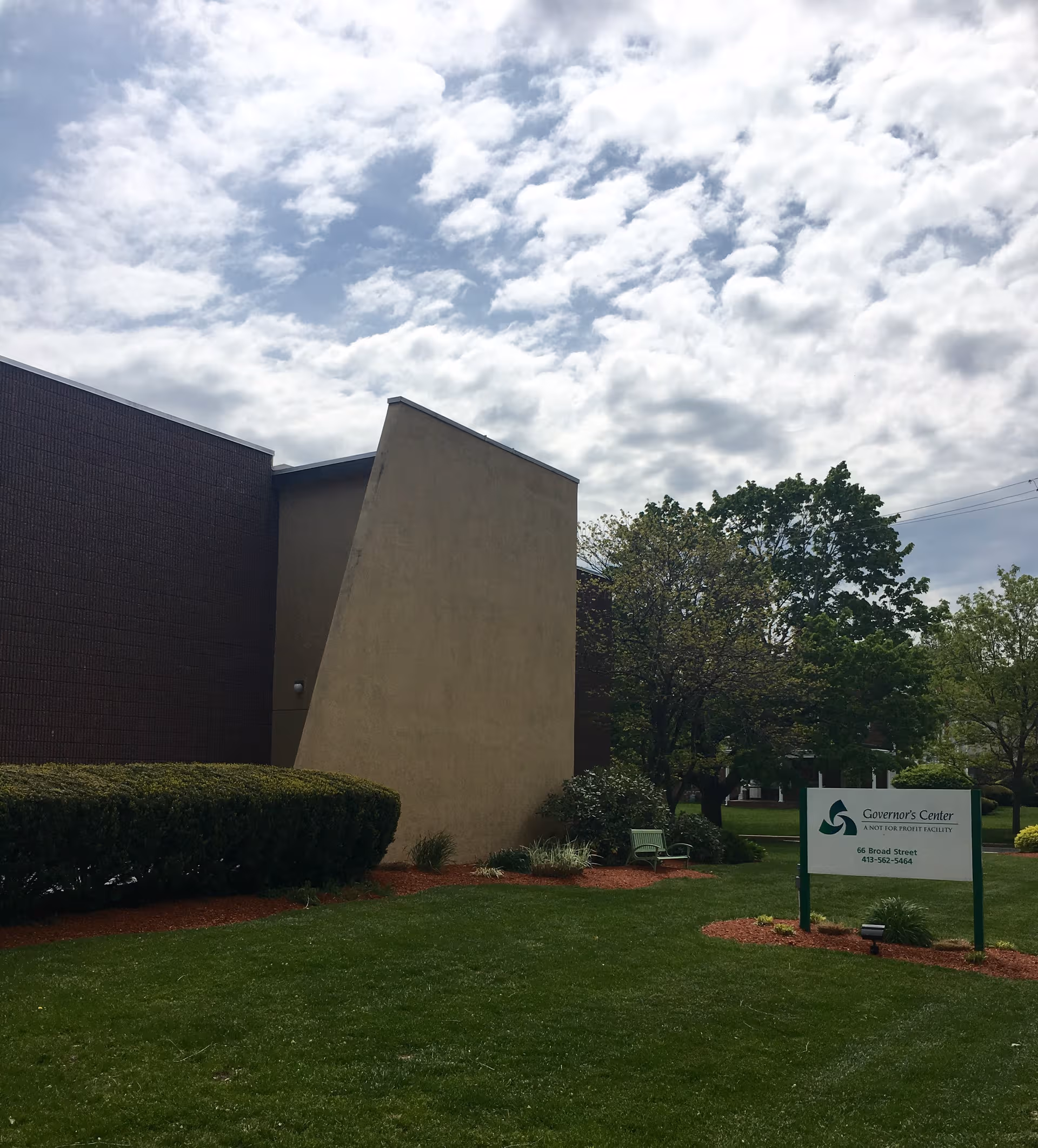 Exterior view of Governor's Center entrance with sign, lawn, and trees.