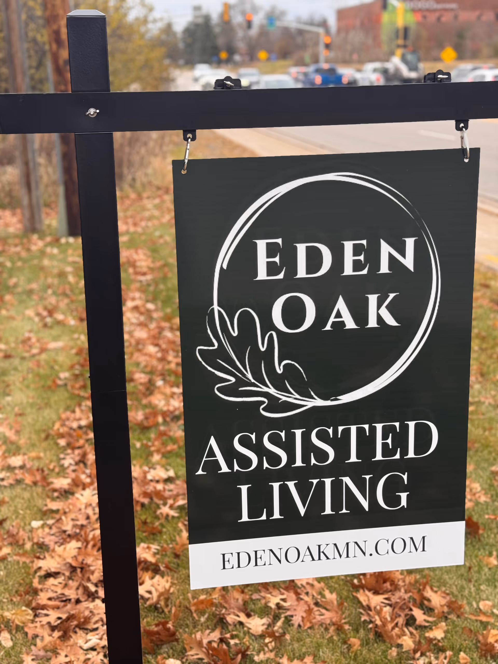 Outdoor sign reading Eden Oak Assisted Living hangs in a leaf-strewn yard.