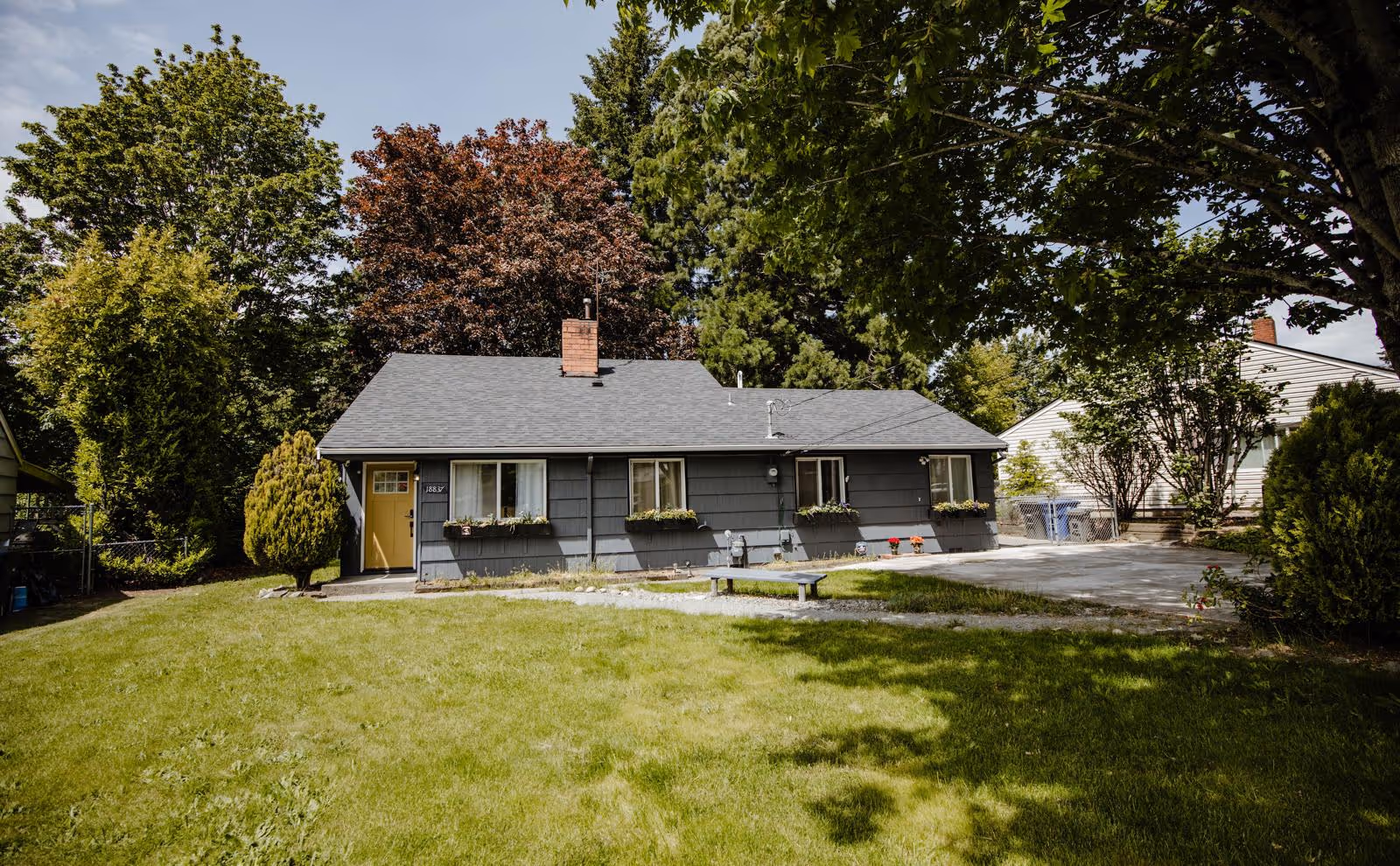 Single-story gray care home with yellow door, flower boxes, and a grassy front lawn.
