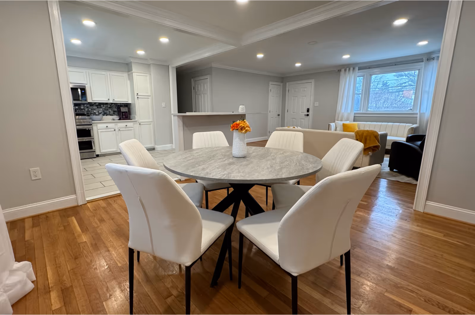 Open-concept dining area with a round table, white chairs, and a visible kitchen in background.