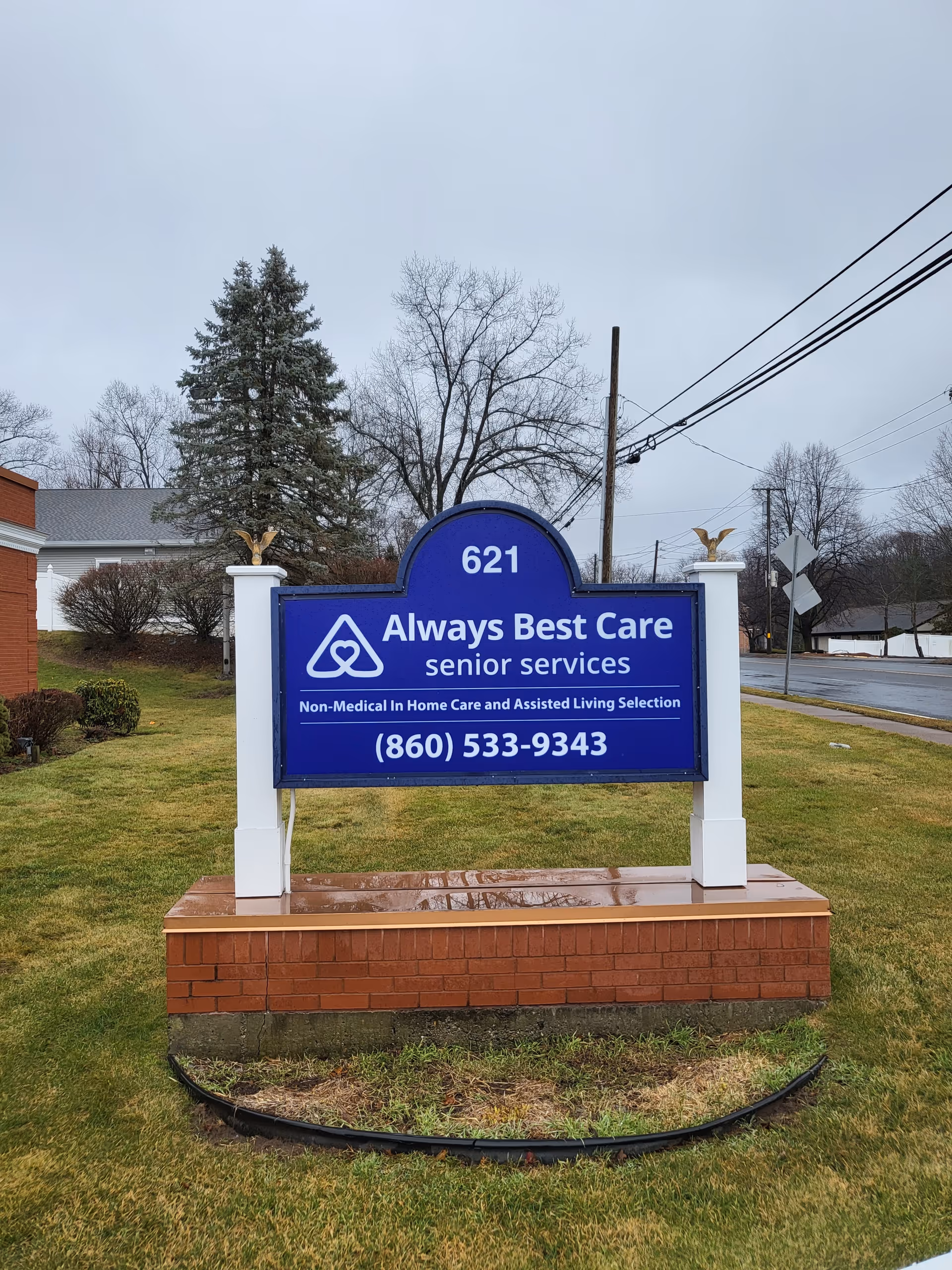 Blue sign for Always Best Care senior services on a pedestal outside a brick base.