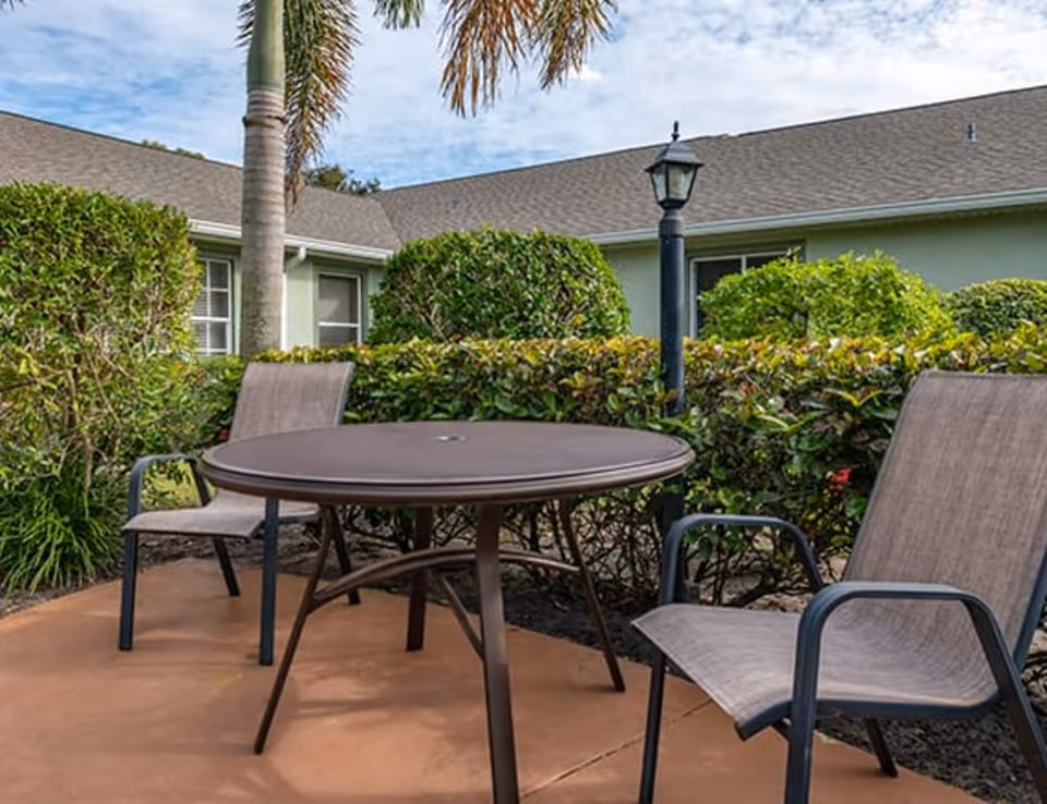 Outdoor patio with round table and chairs amid hedges near a building.