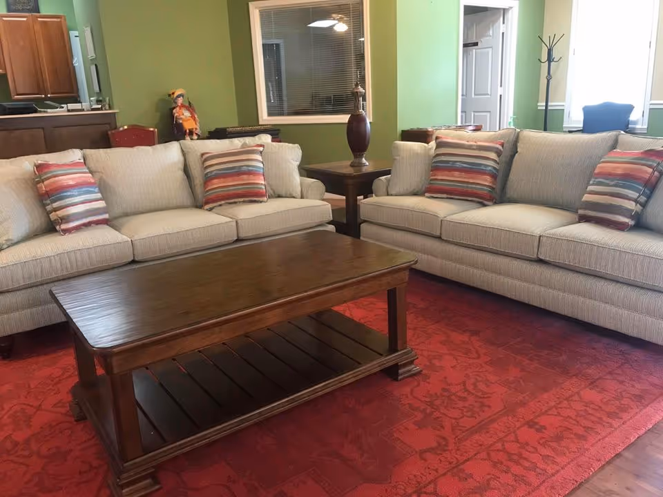 Two beige sofas with striped throw pillows face a wooden coffee table on a red area rug in a green-walled living room.