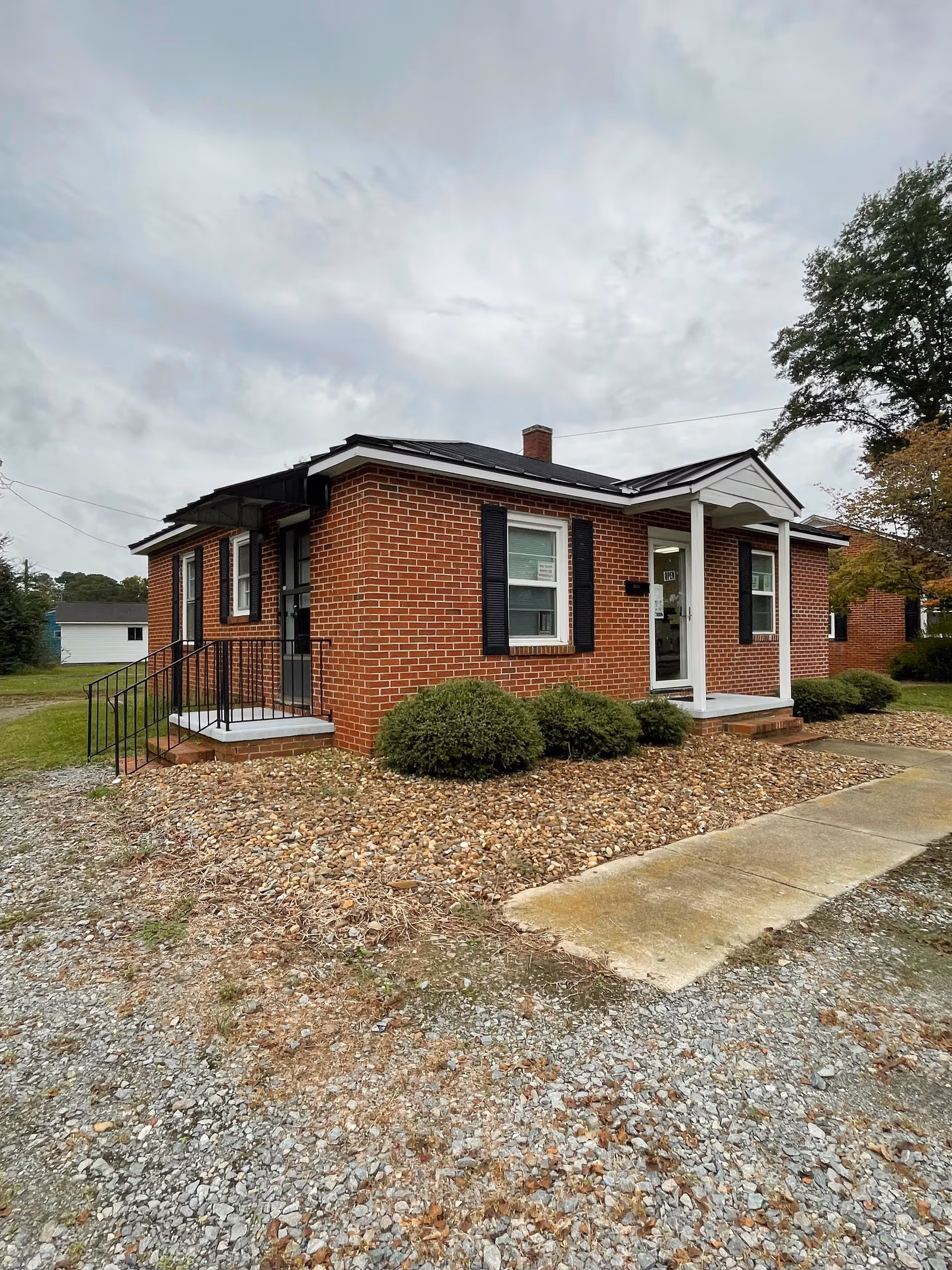 Brick senior living facility exterior with a small front porch, shrubs, and a gravel driveway.