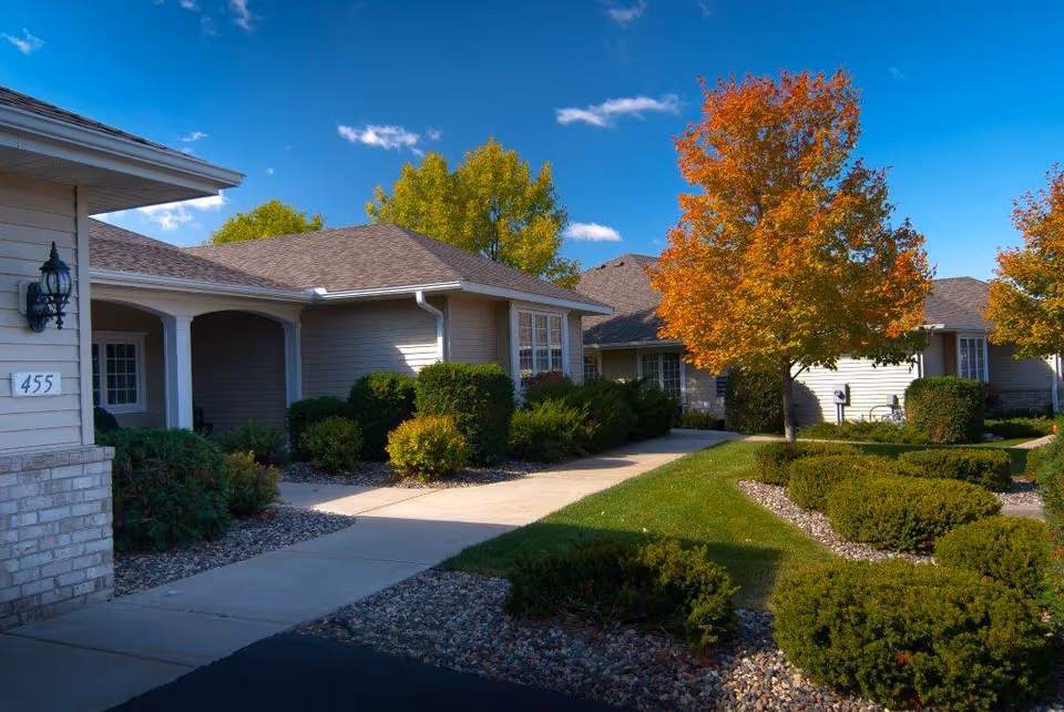 Row of beige, townhome-style senior living buildings with walkways and trees.