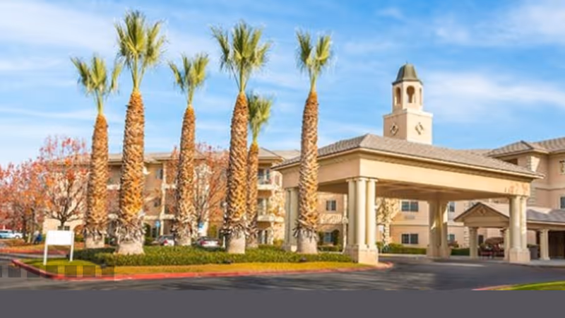 Riverwalk senior living facility exterior with palm trees and a covered entrance.