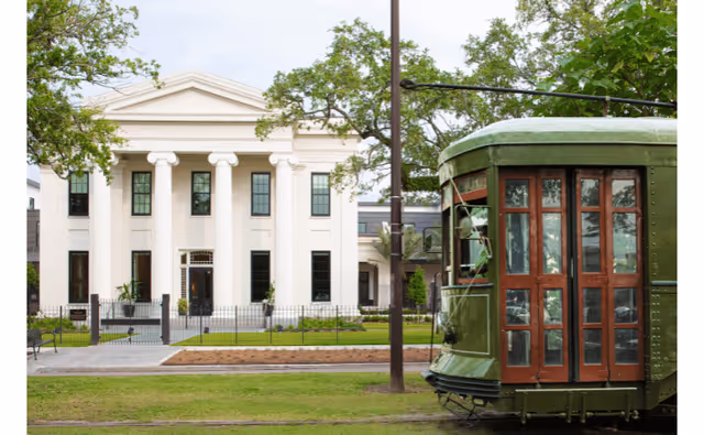 White neoclassical building with tall columns and a vintage green streetcar in front.