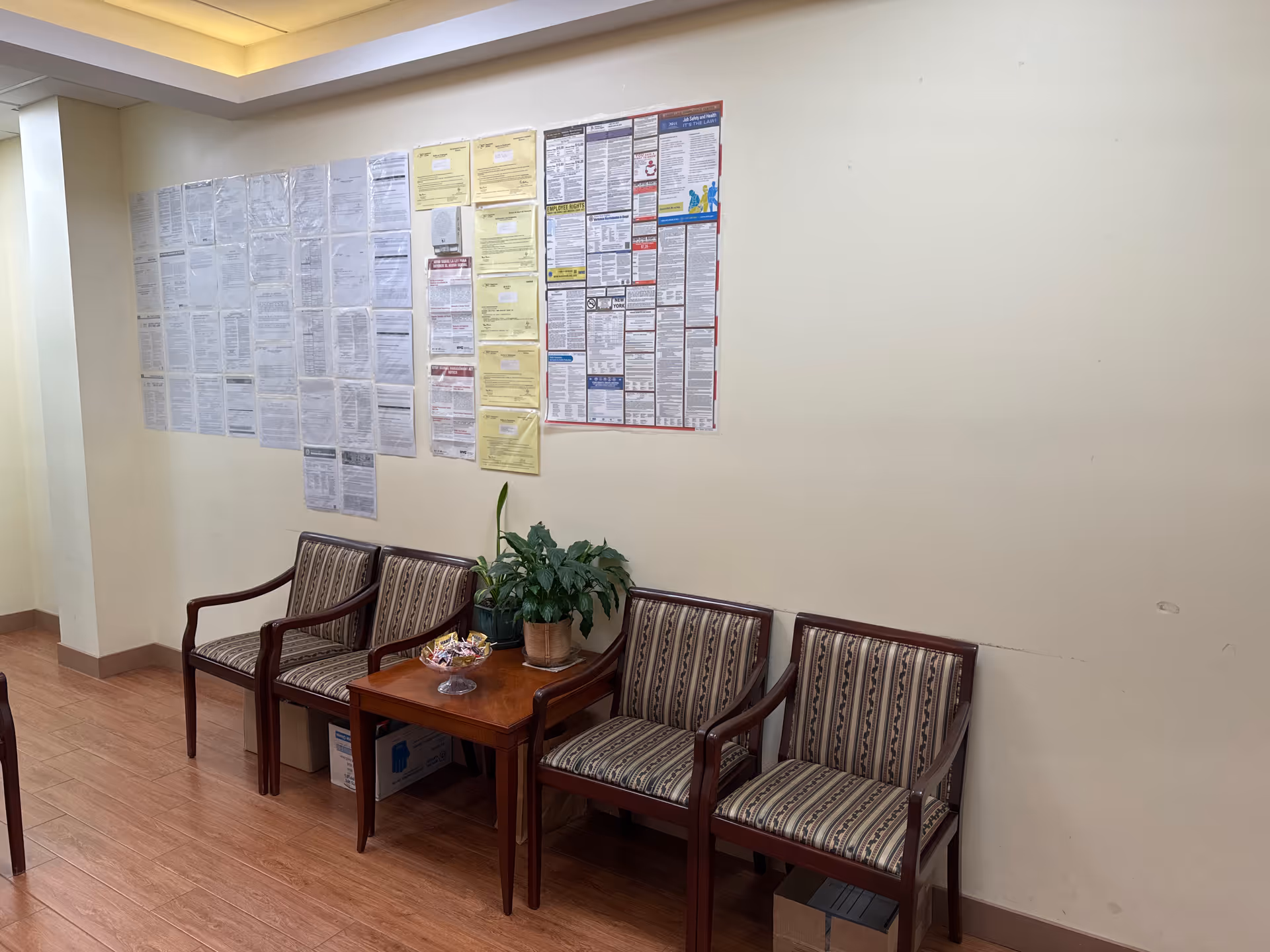 Waiting area with four striped chairs, a table, plant, and wall notices.