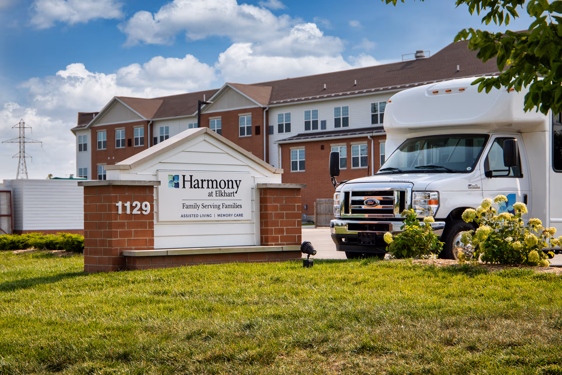 Front view of Harmony at Elkhart facility with sign, building, and a large white bus.