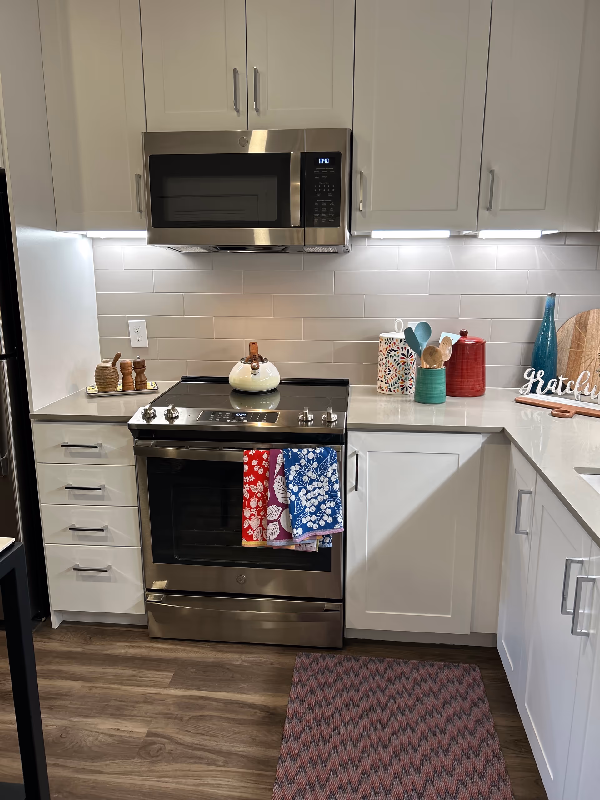 Modern kitchen with stainless steel stove and microwave, white cabinets, and utensils on the counter.
