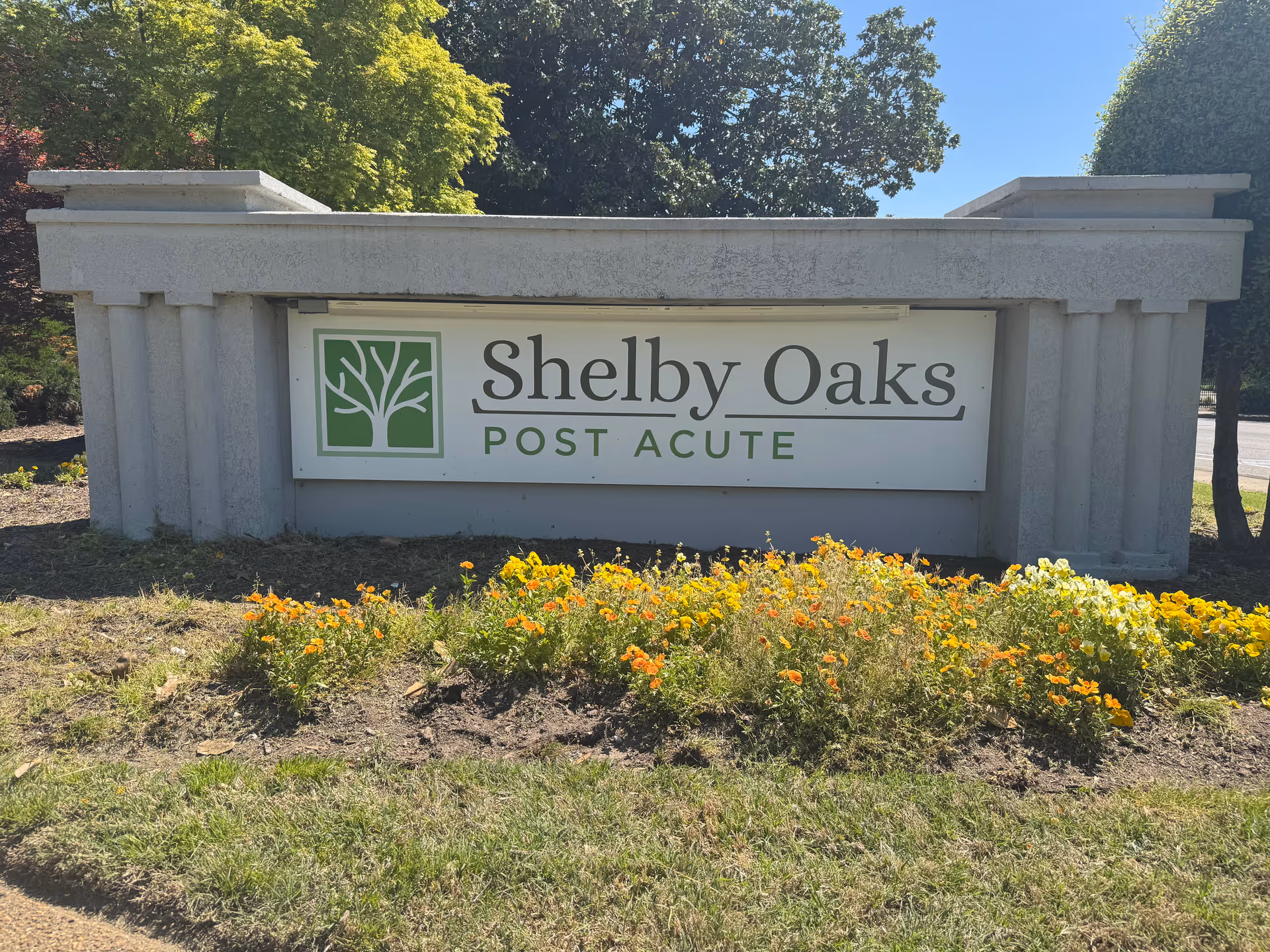 Front view of a concrete sign reading Shelby Oaks Post Acute with flowers in front