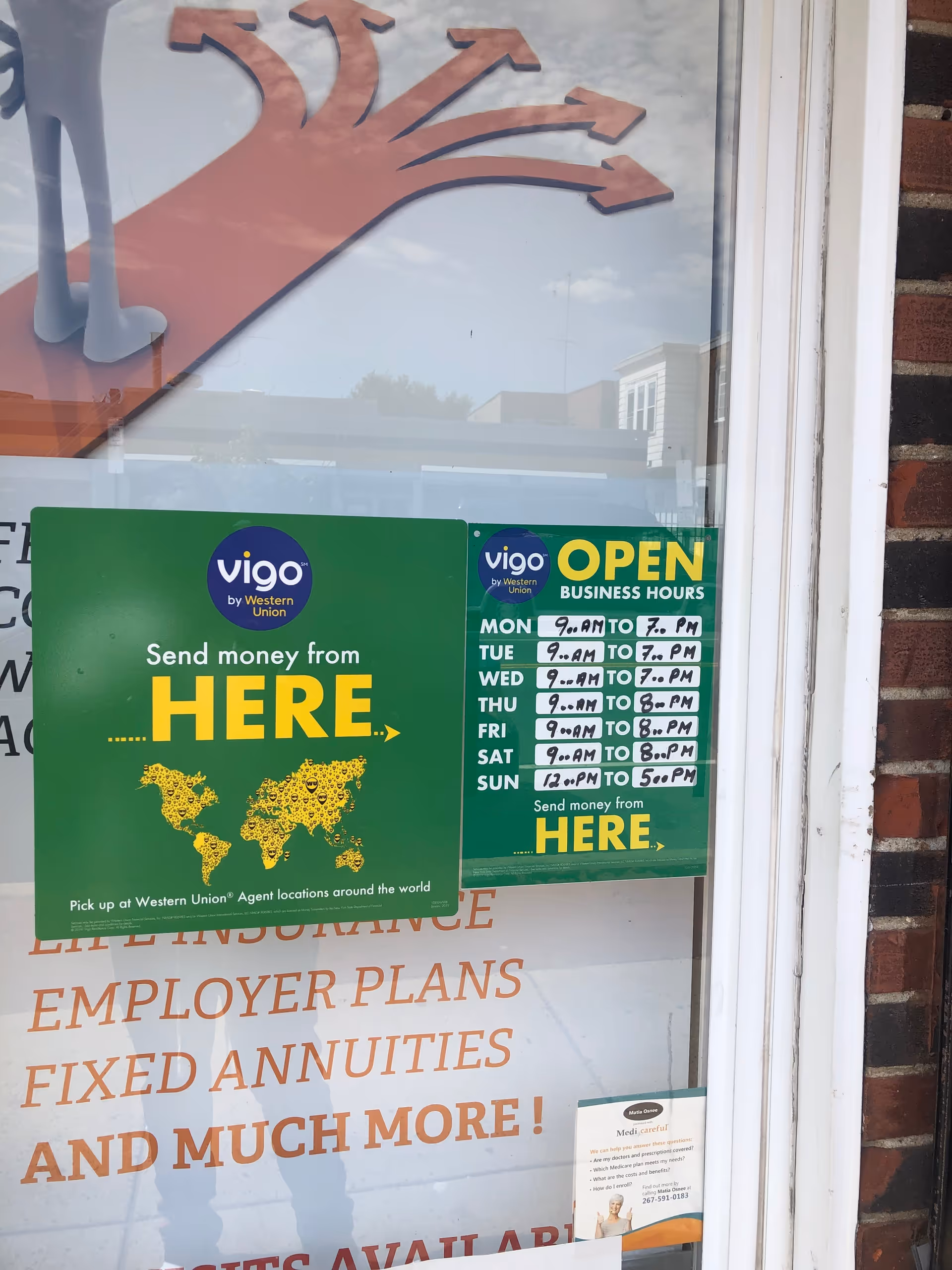 Storefront window displaying Vigo money transfer signs and business-hours poster