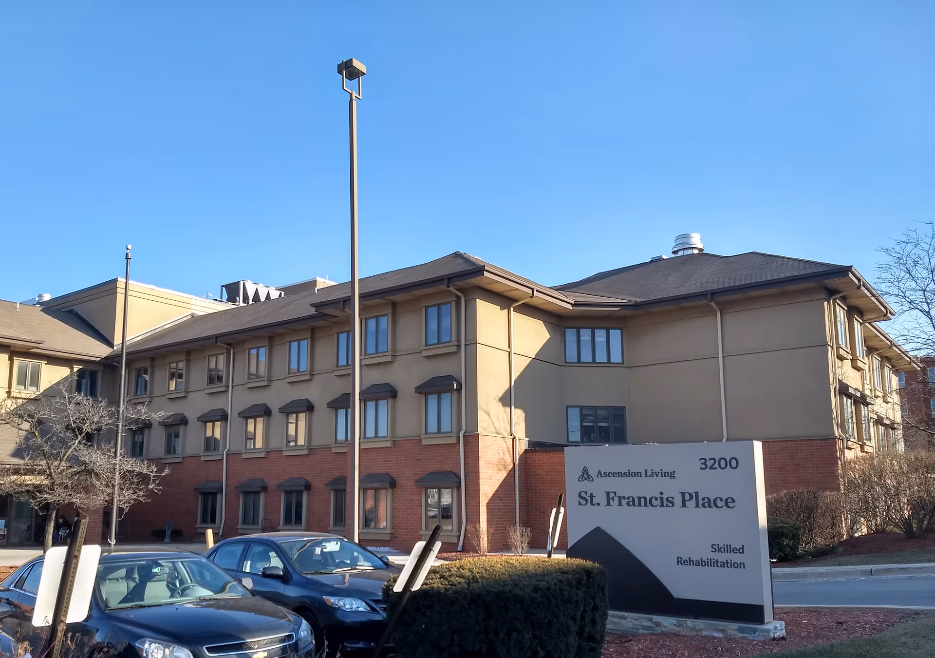 Exterior view of Ascension Living St. Francis Place with building, sign, and parked cars.