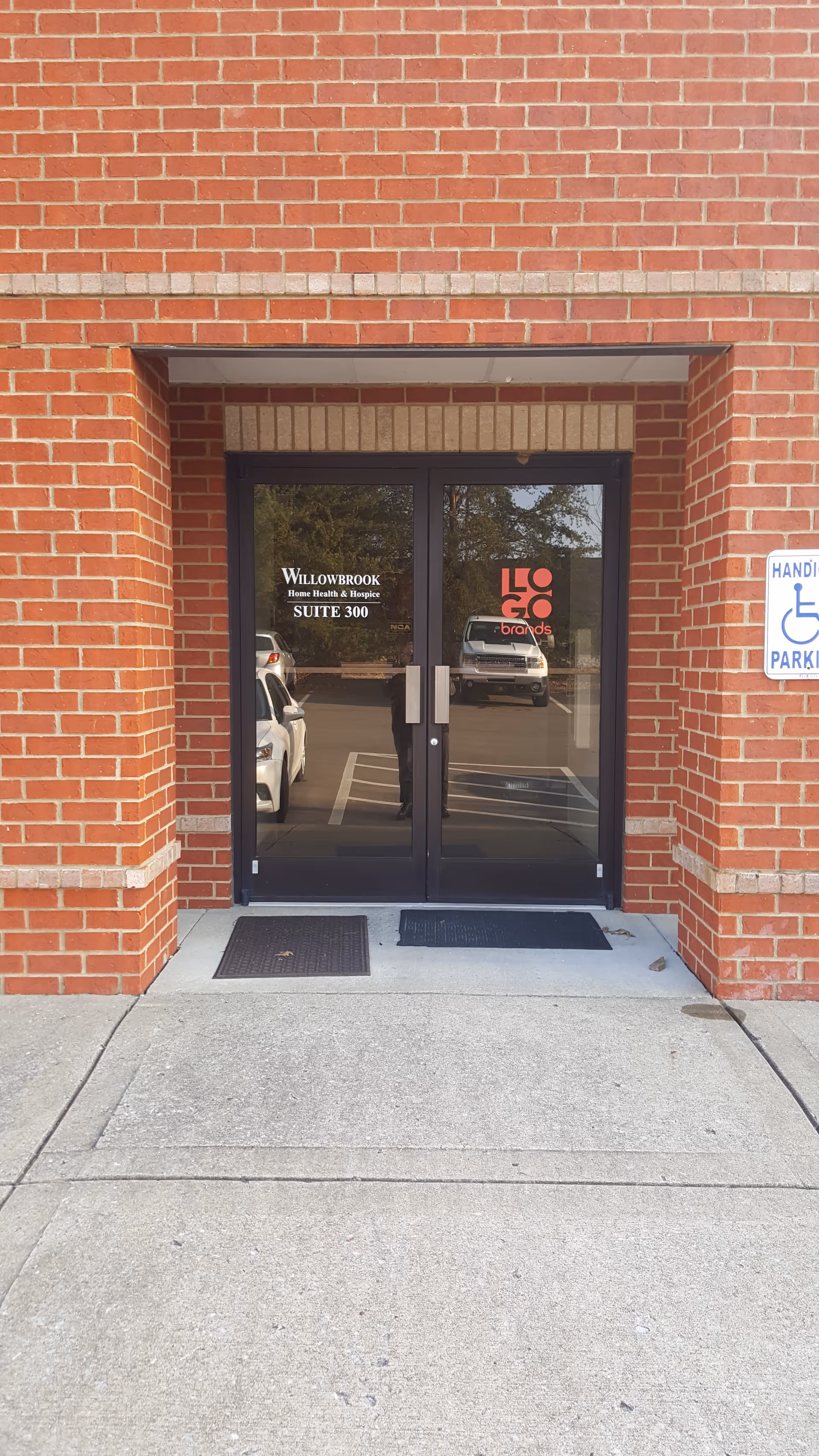 Exterior brick building entrance with glass doors and a handicap sign.