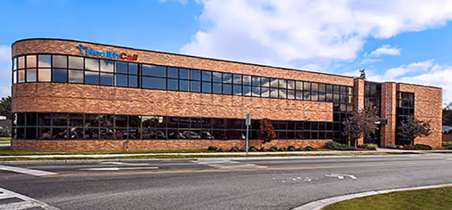Two-story brick HealthCall facility exterior with large front windows and blue sky.