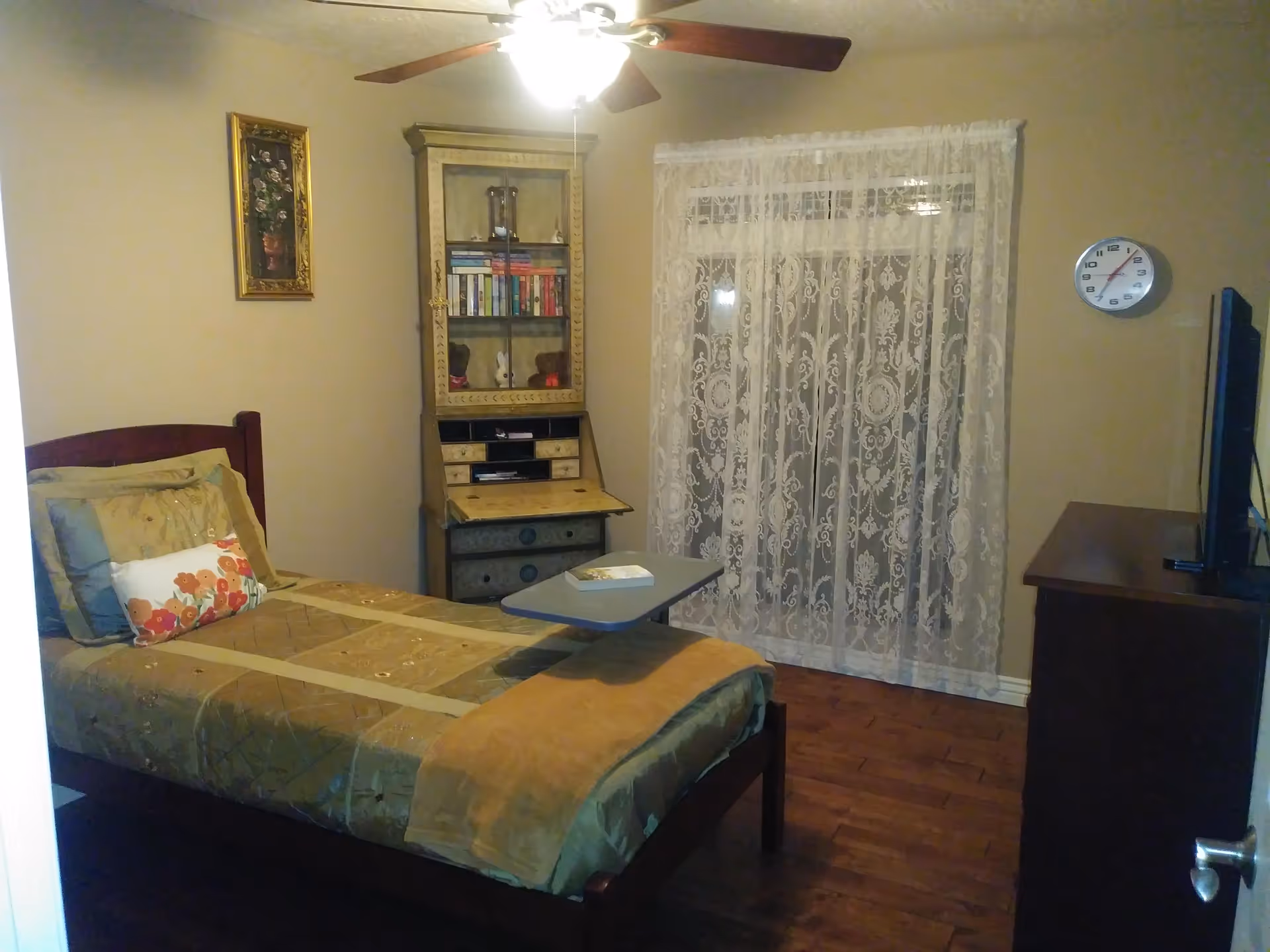 A cozy bedroom with a bed, dresser, lace curtain, and ceiling fan