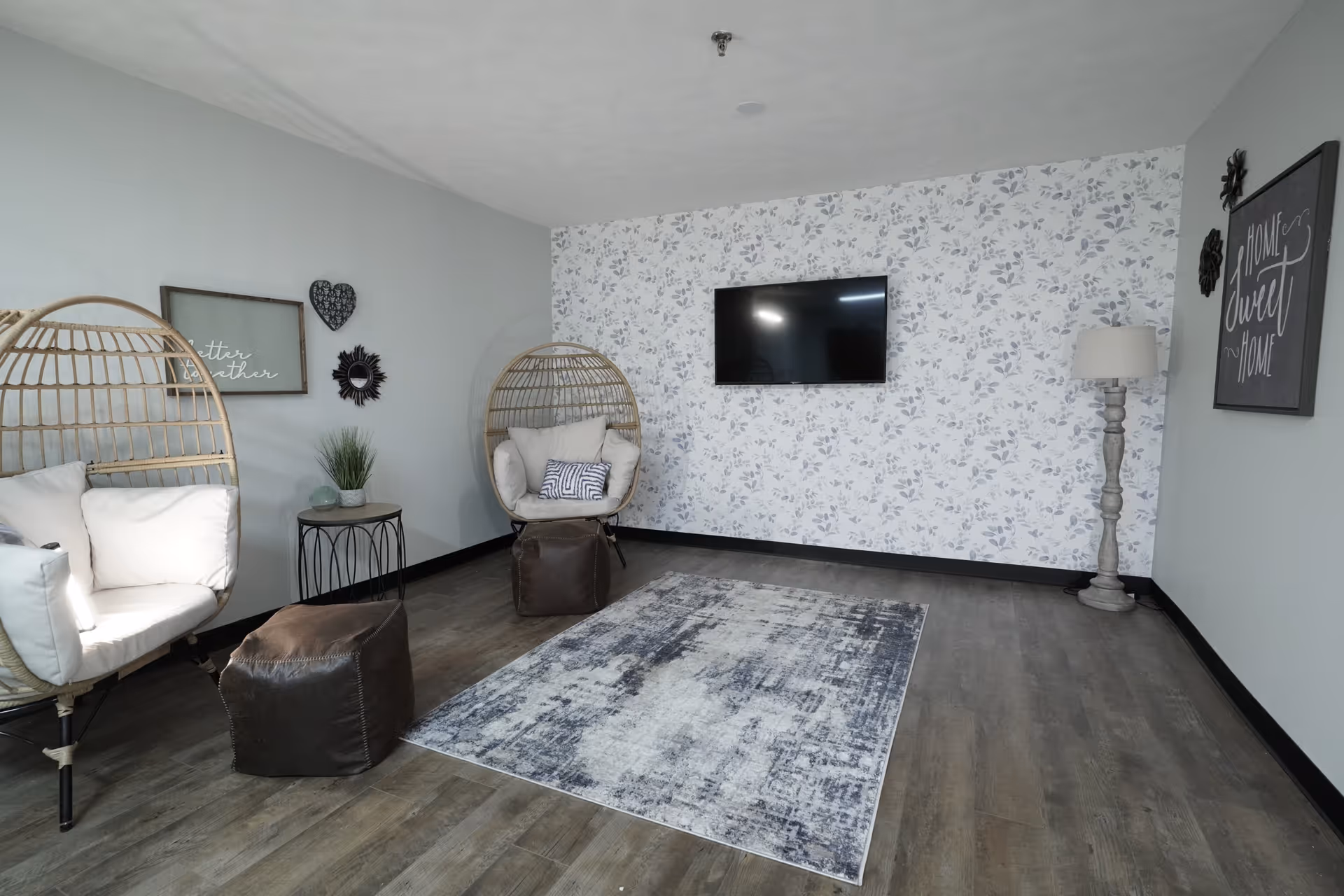Cozy lounge area with wicker chairs, rug, flatscreen TV, and floral wallpaper.