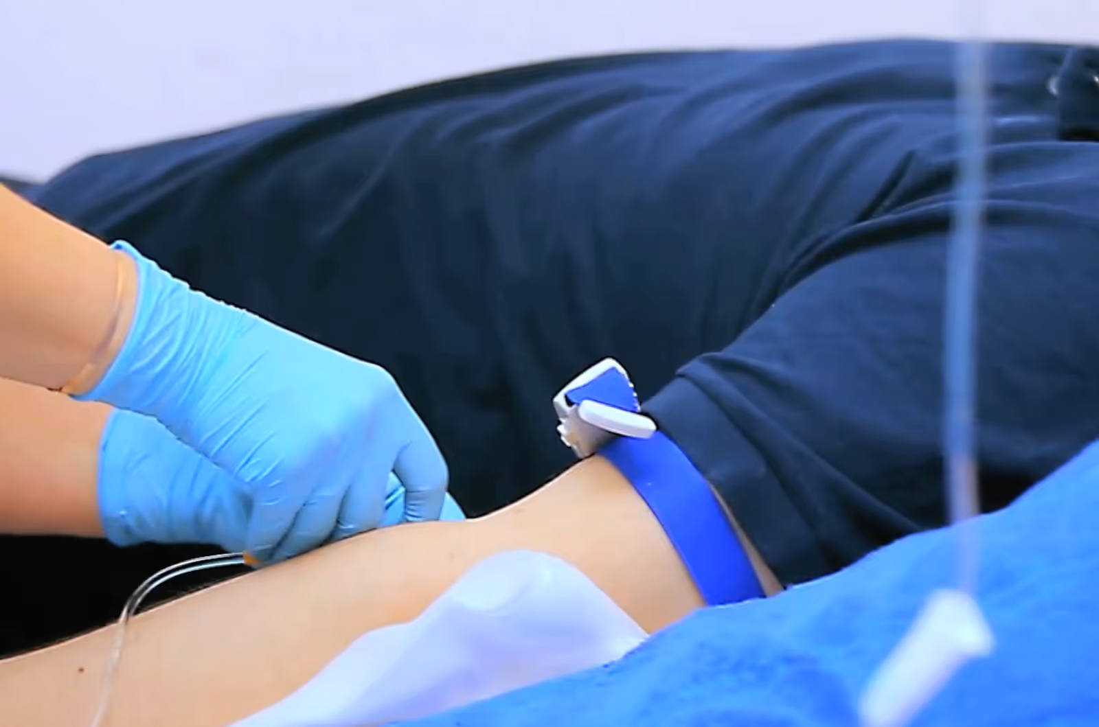 Medical professional with blue gloves performs IV insertion on a patient's arm.