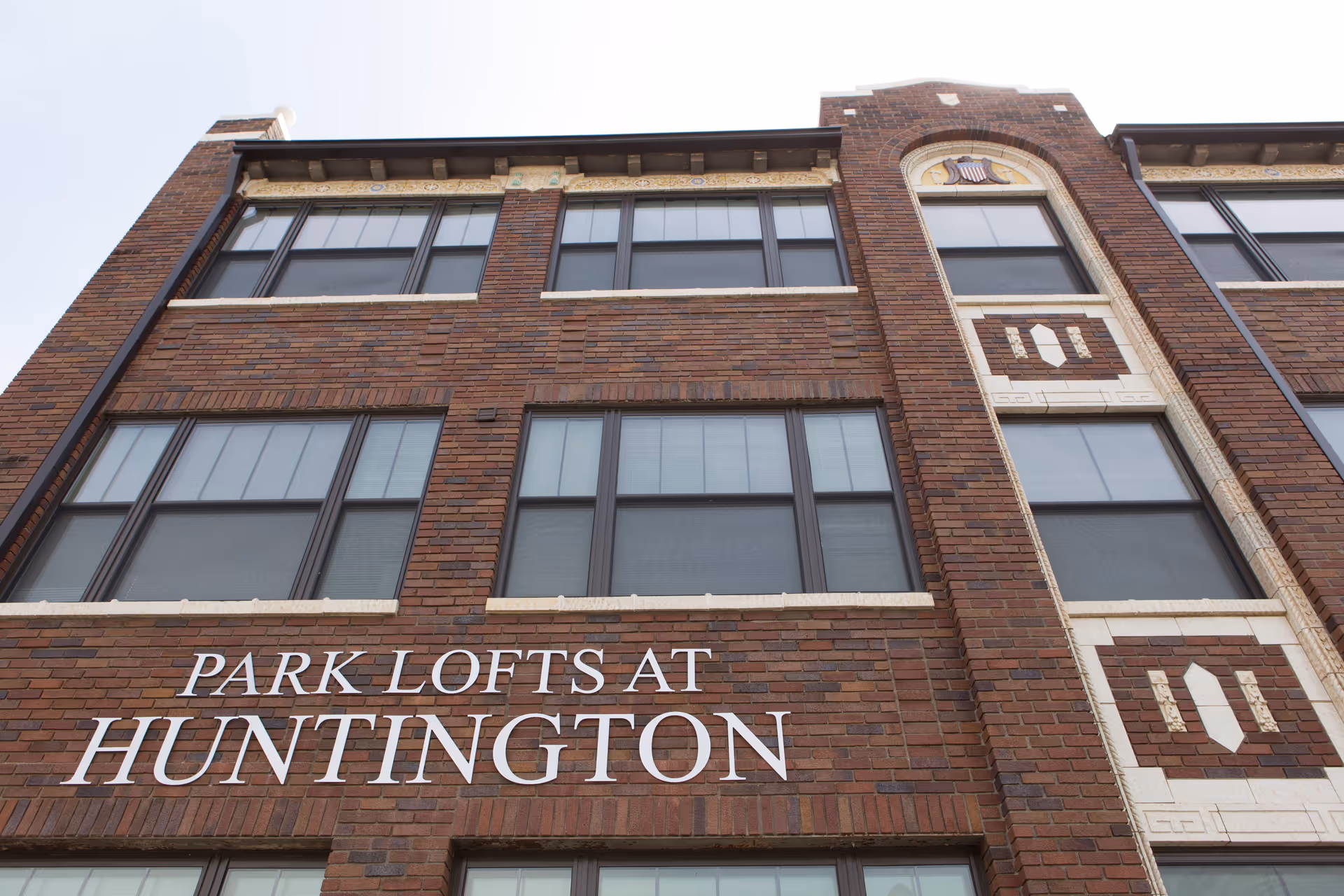 Exterior view of a brick building with multiple windows and decorative stonework, featuring the sign 'Park Lofts at Huntington' on the facade.
