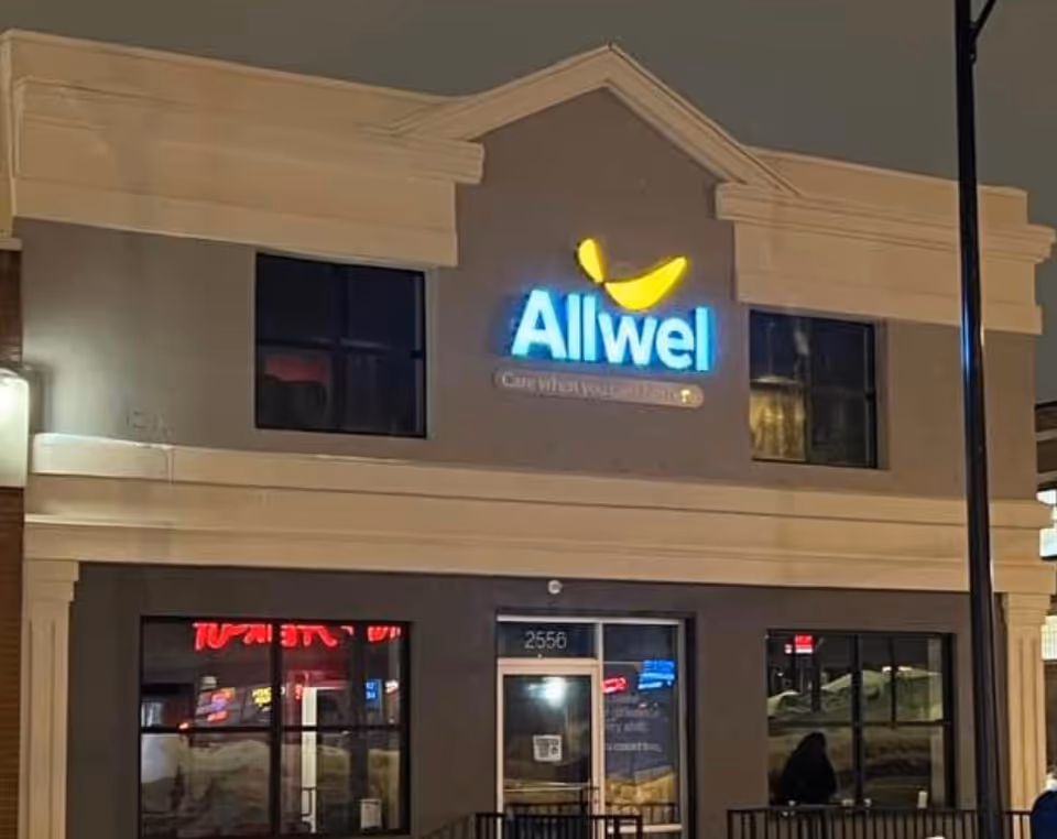 Night exterior of an Allwel senior living building with a bright blue sign.