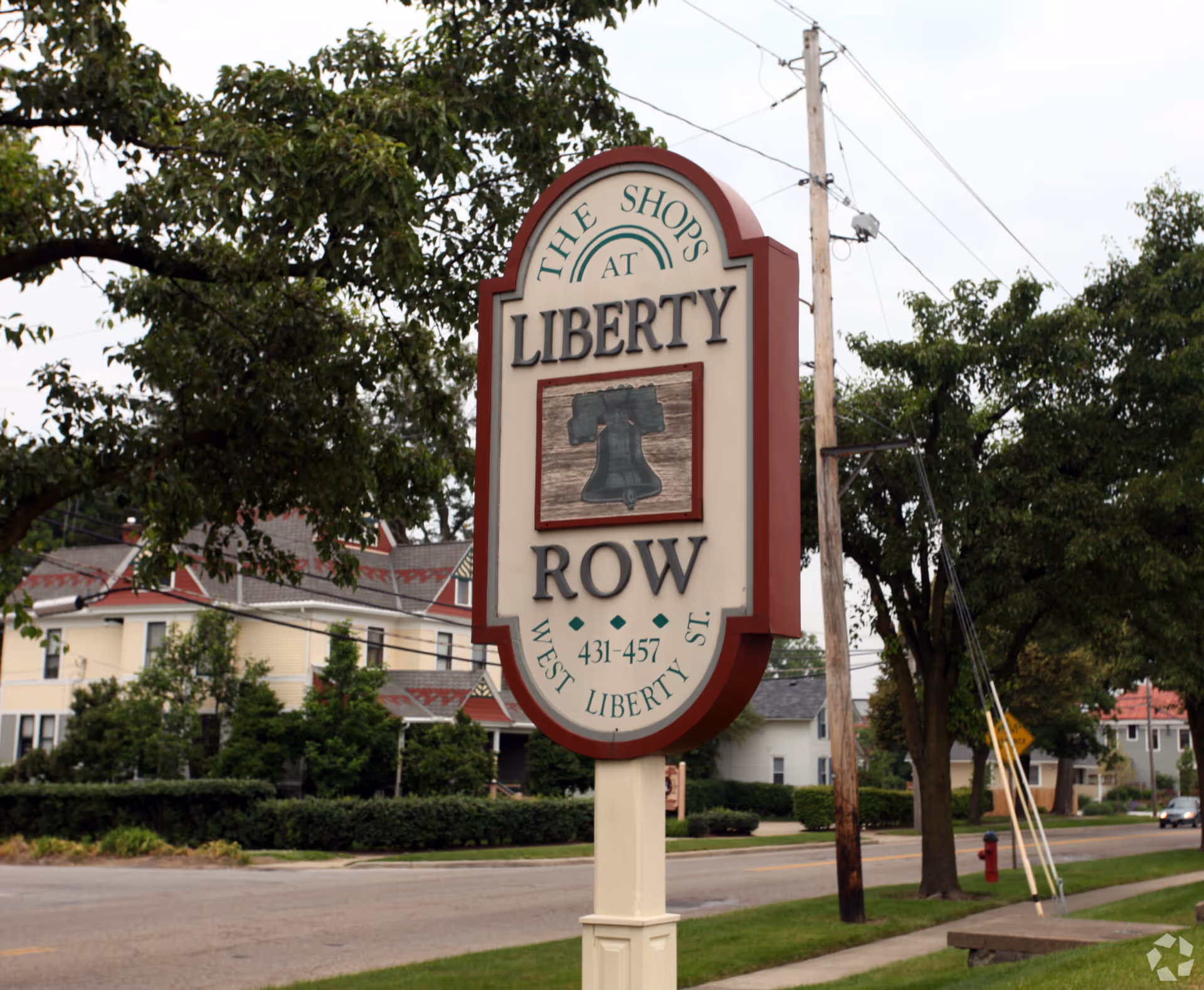 A roadside sign reads The Shops at Liberty Row with trees and houses in background