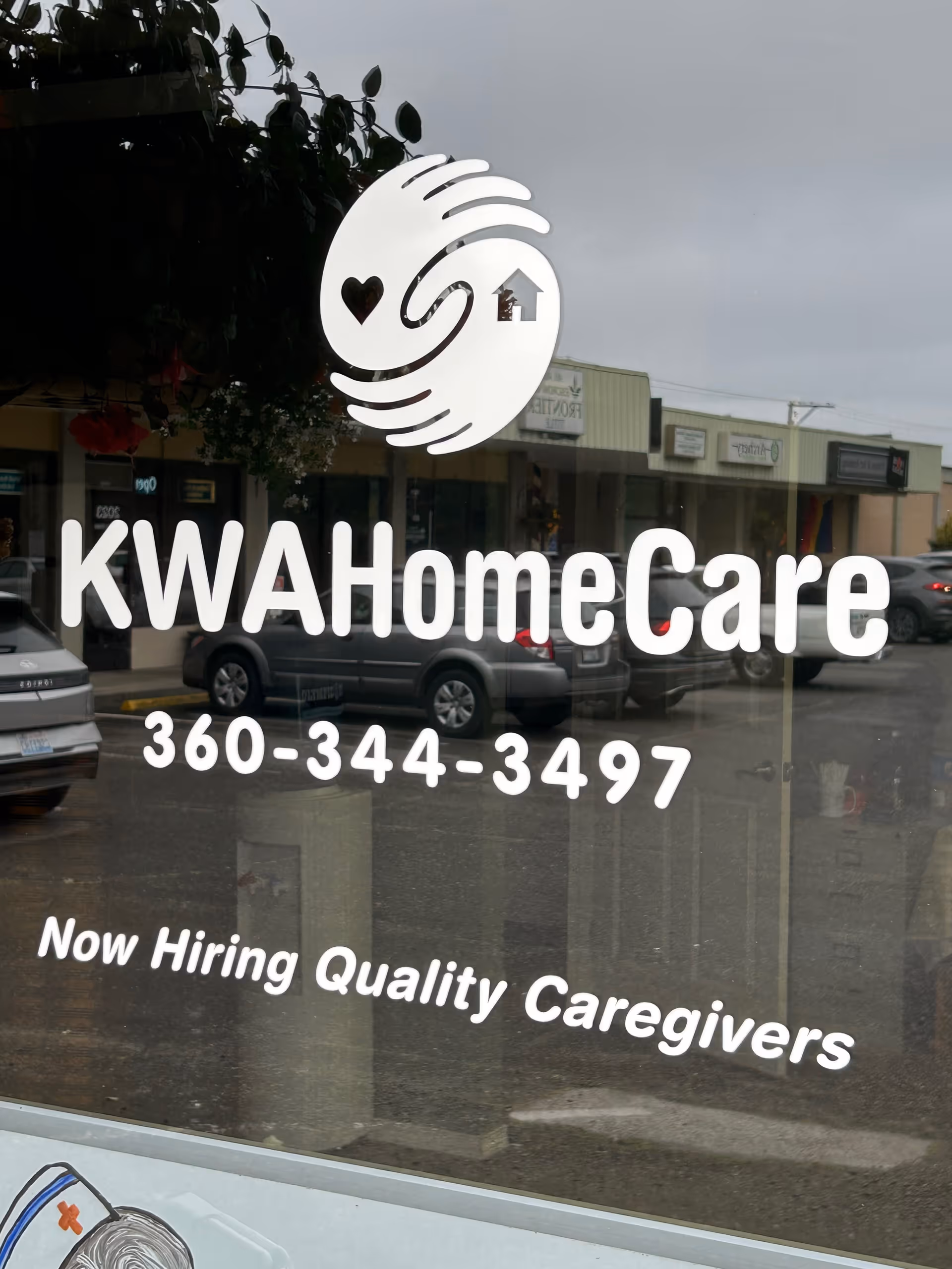 Glass storefront window shows KWA HomeCare logo and 'Now Hiring Quality Caregivers'.